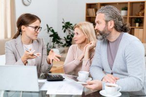 A woman is talking to a man and woman while sitting at a table.