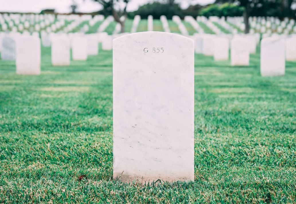 A gravestone in a cemetery with a lot of graves in the background.