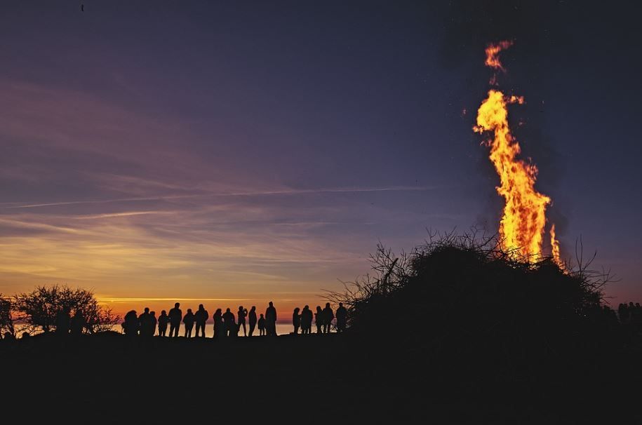 A group of people are standing in front of a large fire at sunset.