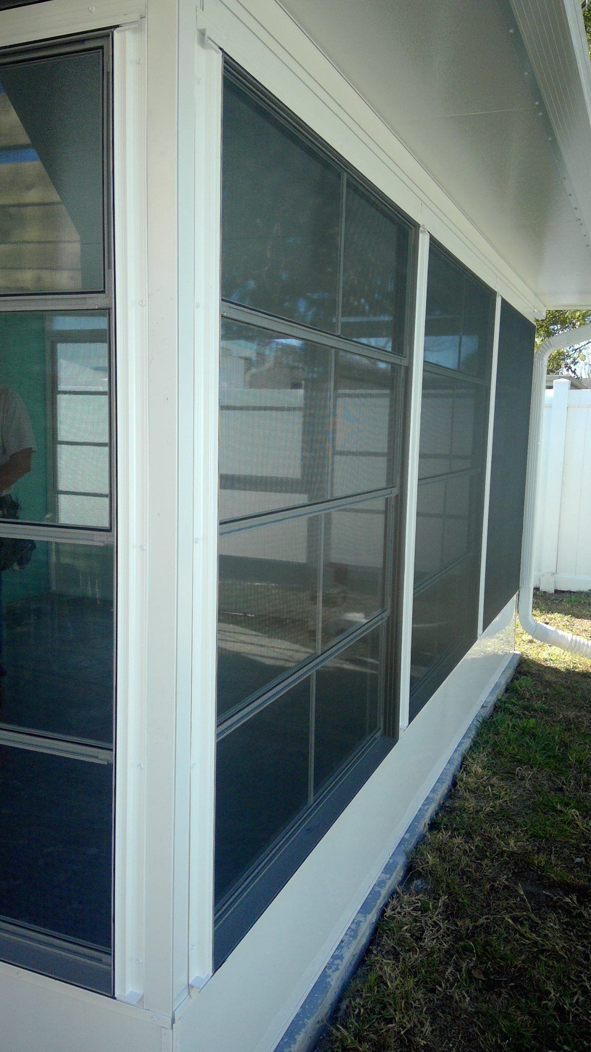 White-framed screened windows on a building's exterior, with a white base, grass, and a white fence visible.