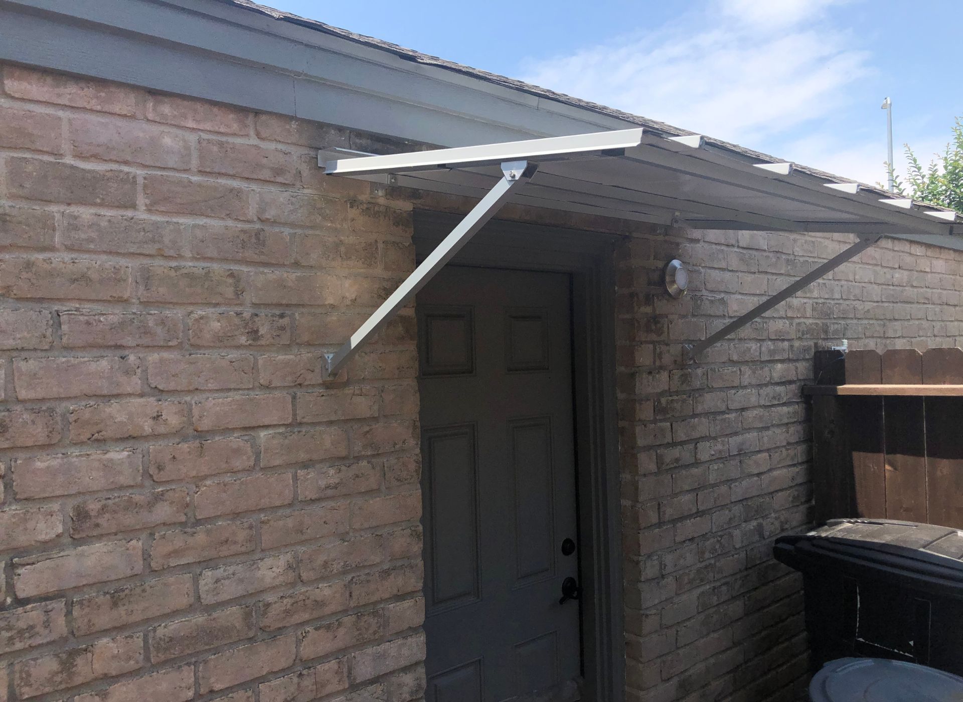 Brick building with white metal awning above a gray door; trash can visible.