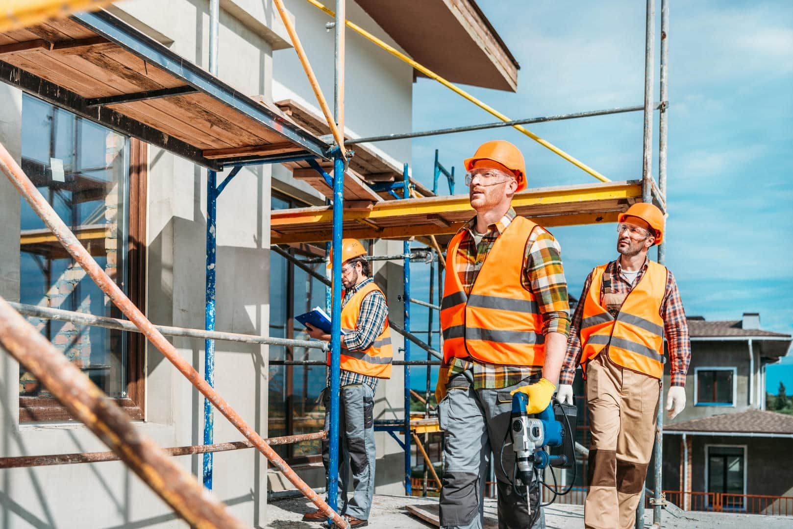 Construction workers on scaffolding, wearing hard hats and safety vests, working on a building.