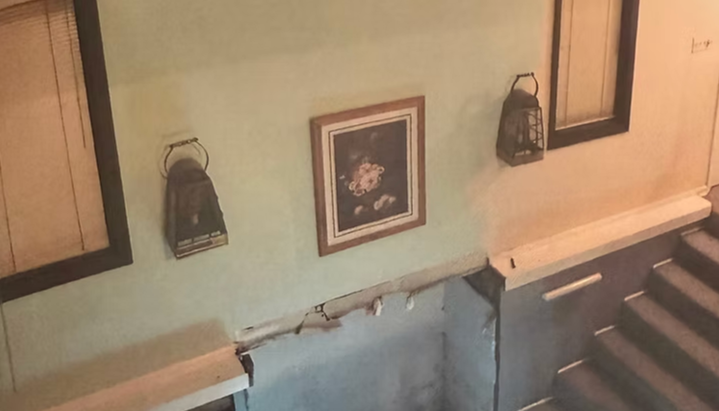 Wall with art and lanterns, by stairs. Pale green wall, wooden frame art. Two dark lanterns hang.