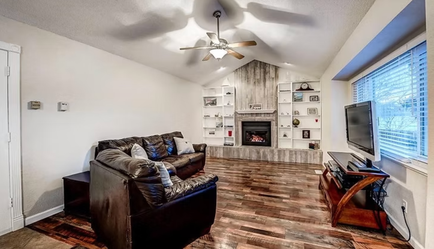 Living room with fireplace, built-in shelves, sofa, TV, and wooden flooring.