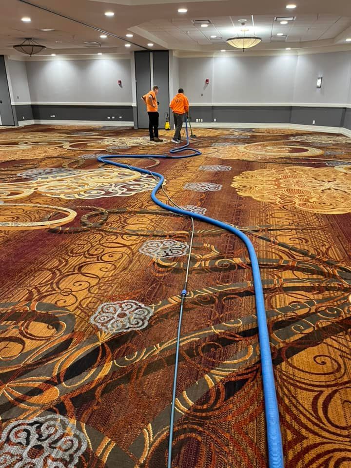 Two men are cleaning a large carpet in a large room.