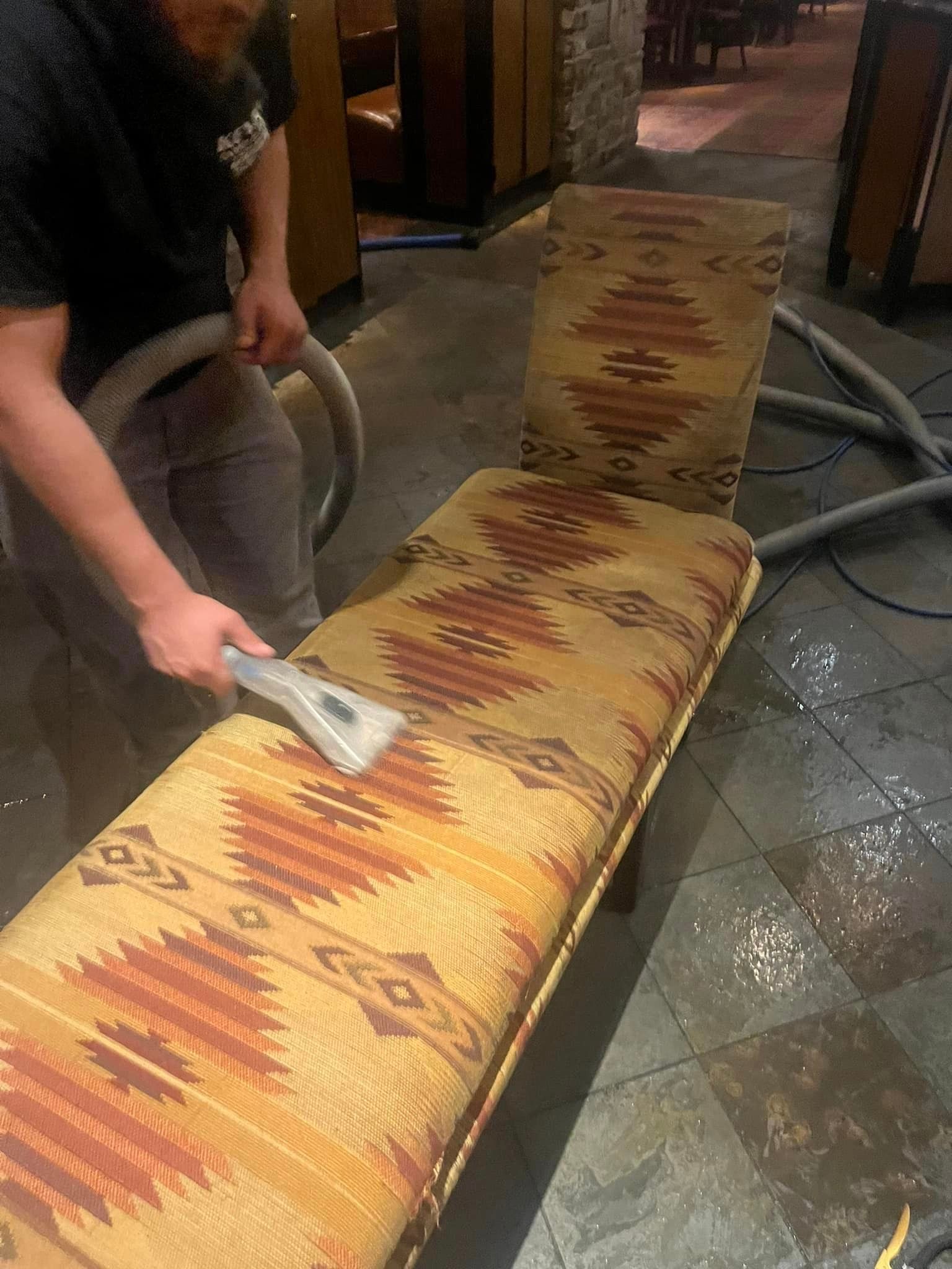 A man is cleaning a chair with a vacuum cleaner.