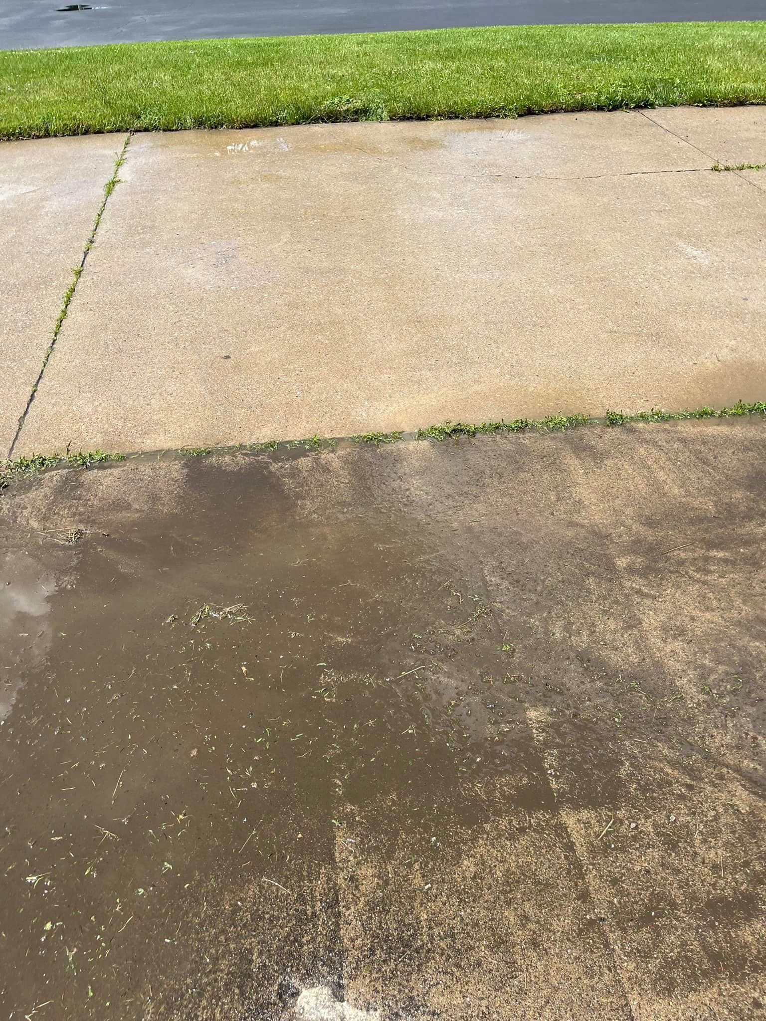 A puddle of water on a sidewalk next to a grassy area.