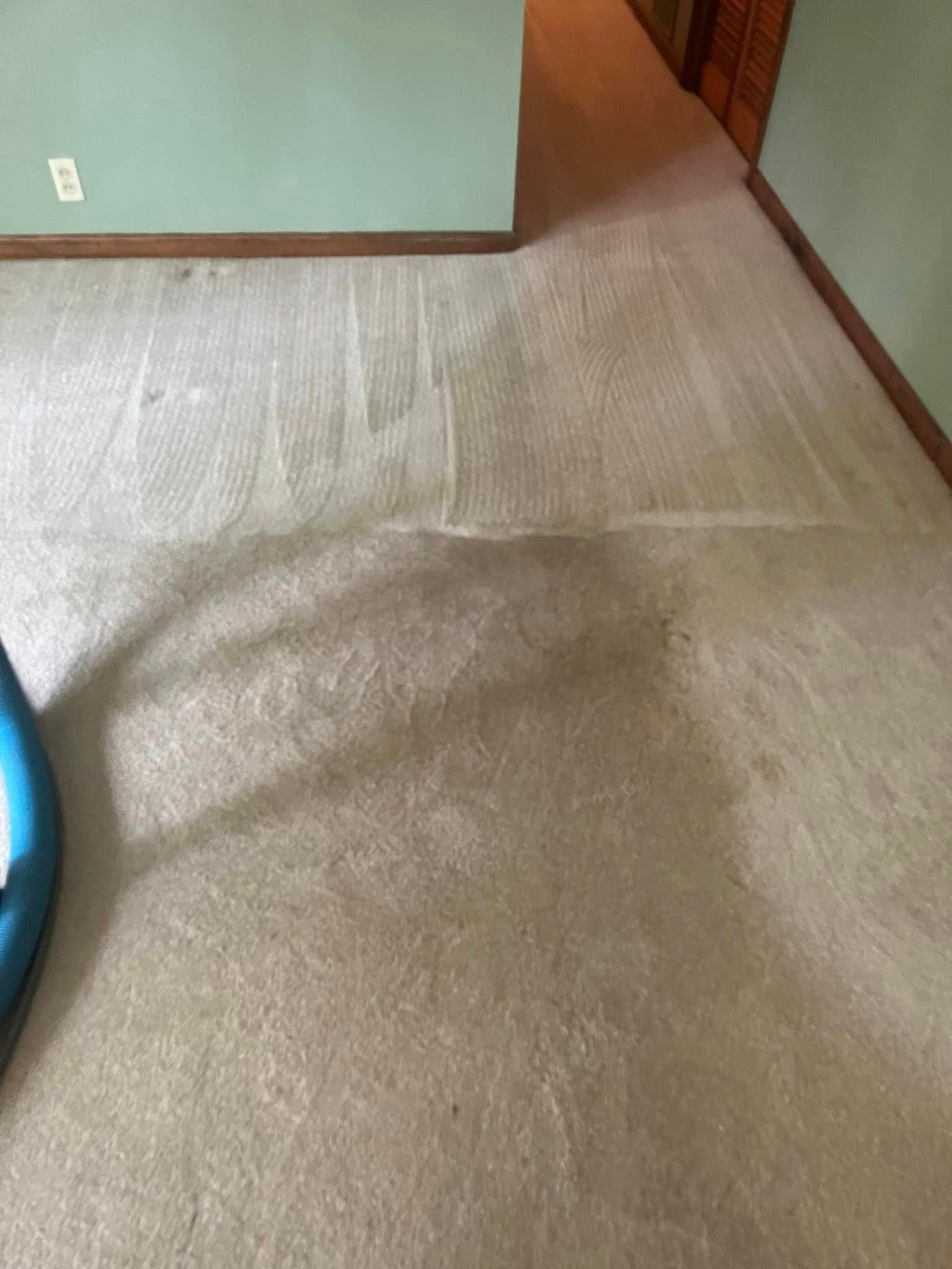 A dirty carpet in a living room with a blue ball on the floor.