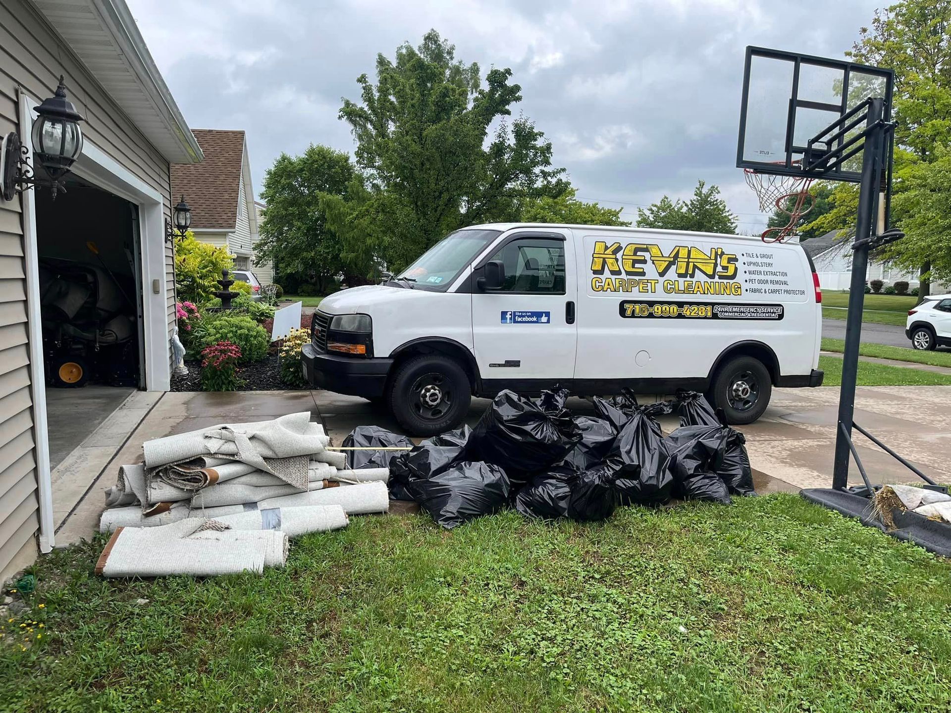 A white van is parked in front of a garage next to a basketball hoop.