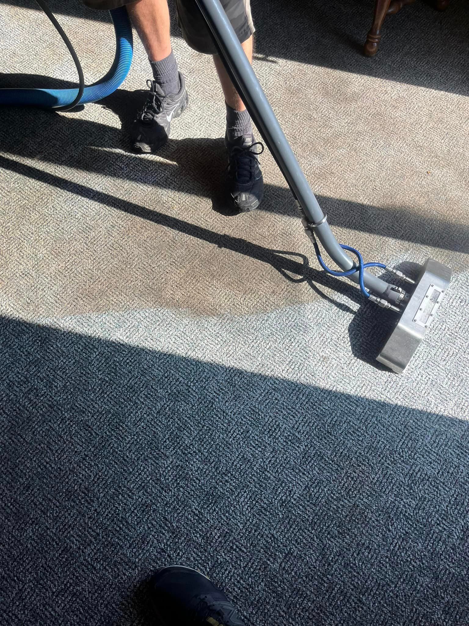 A person is cleaning a carpet with a vacuum cleaner.
