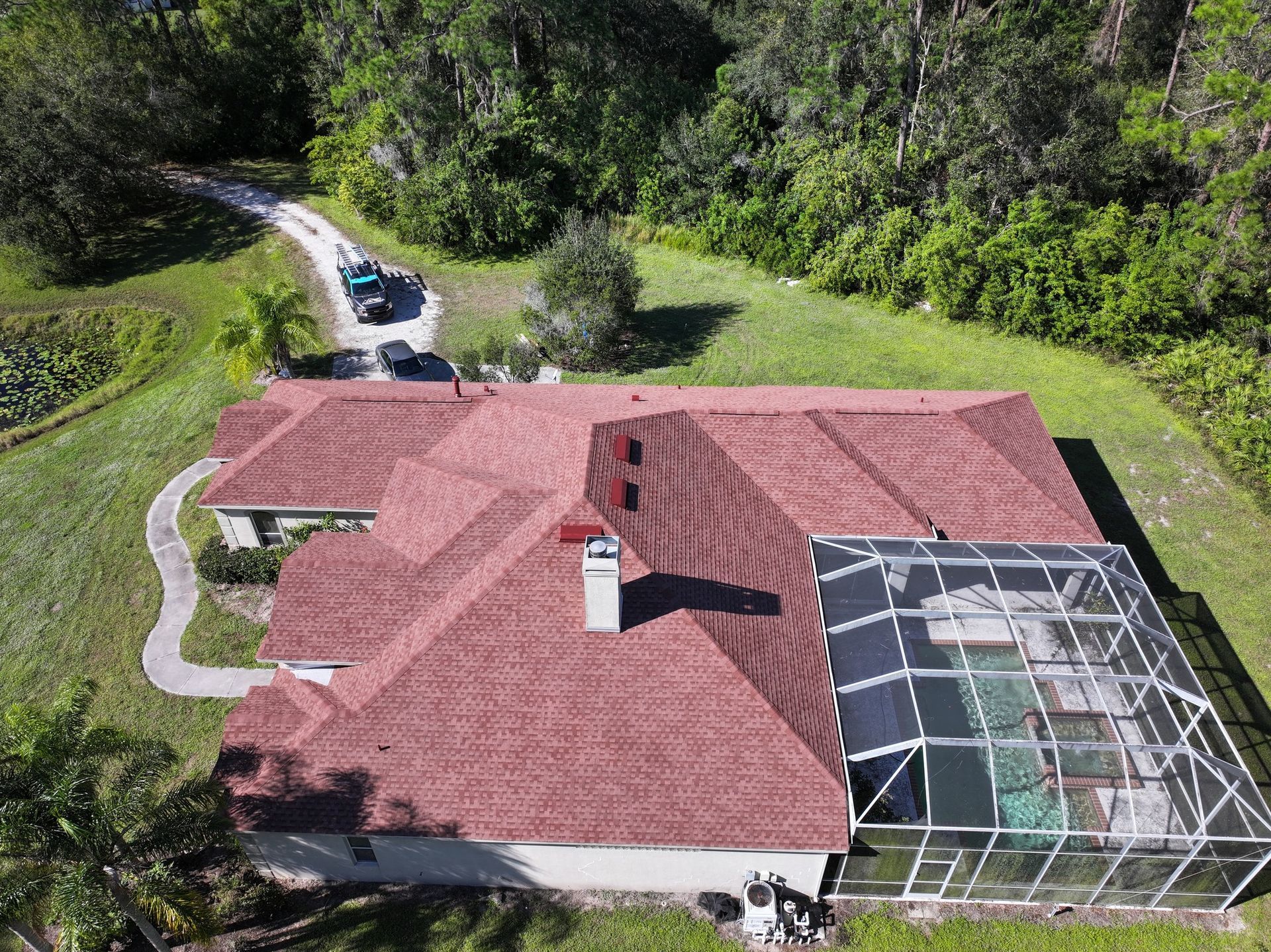 An aerial view of a house with a red roof and a screened in pool.