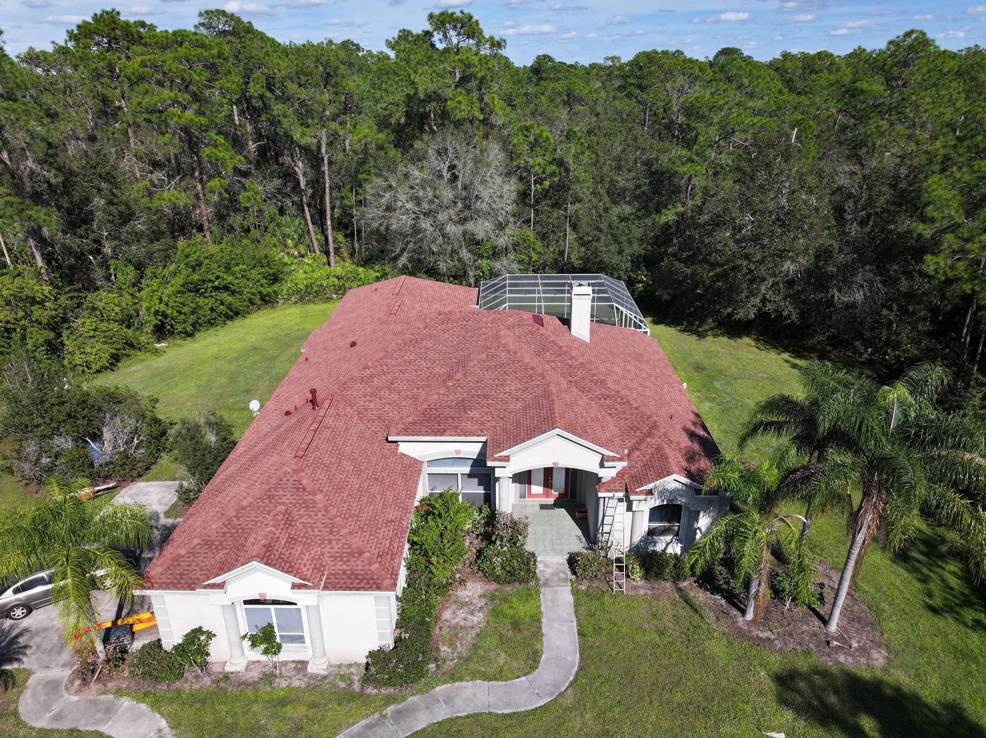 An aerial view of a house with a red roof surrounded by trees.