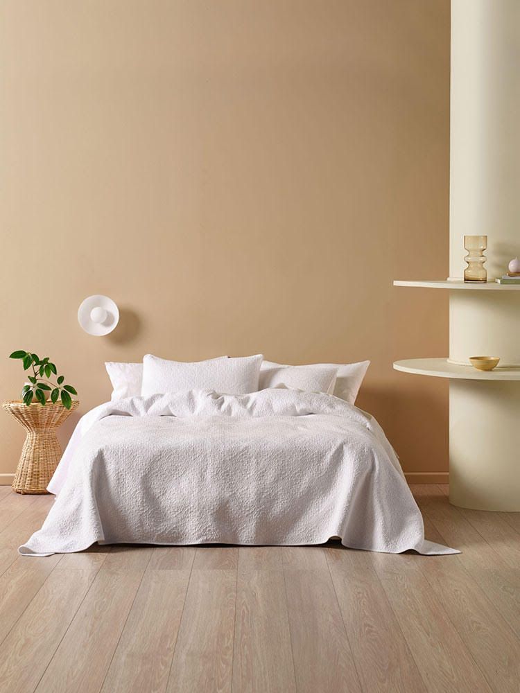 A bed with a white comforter and pillows in a room with a brown wall.