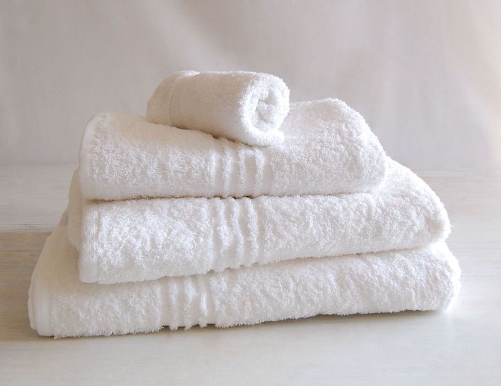 Stack of white towels on a light-colored surface. One is rolled on top.