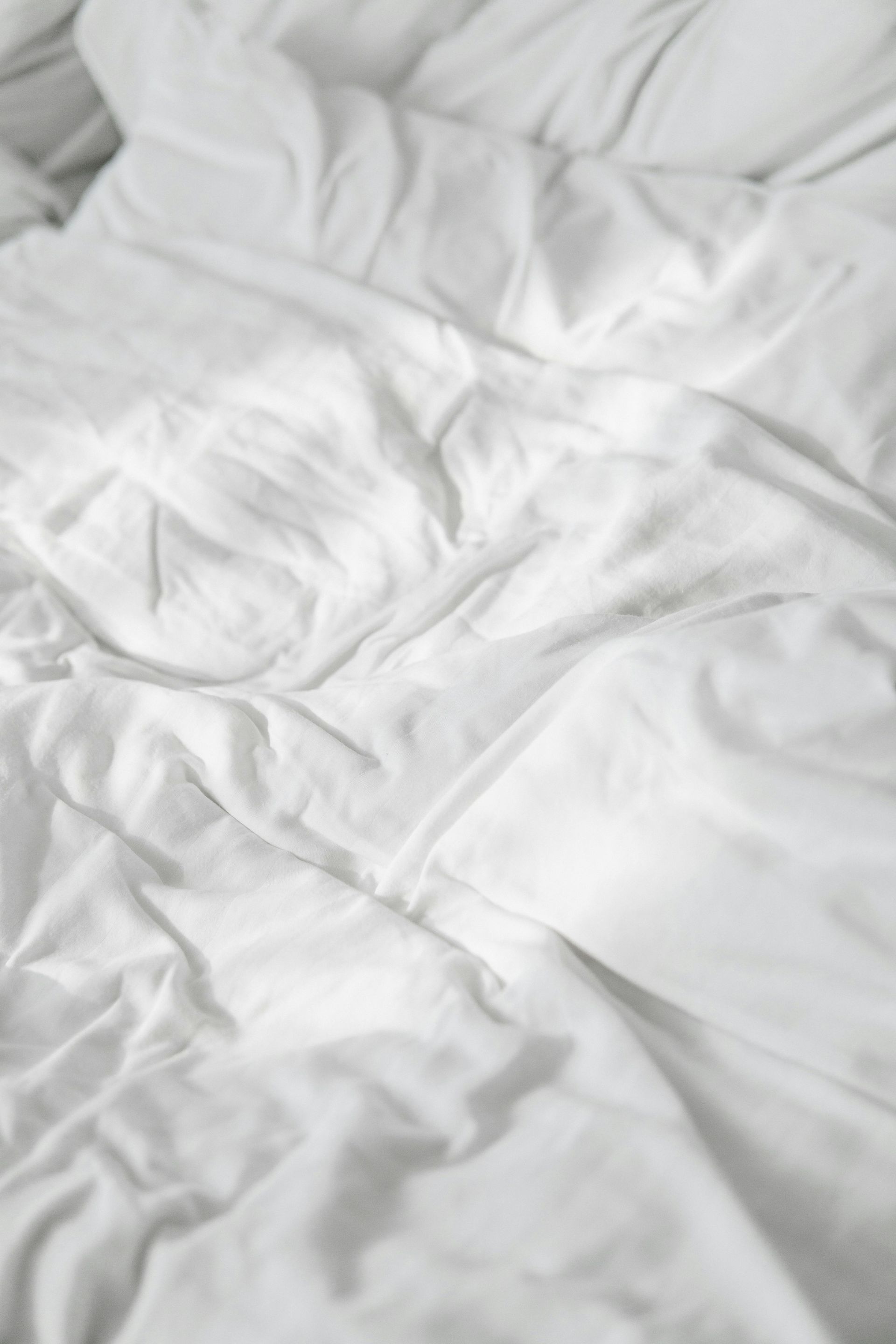 Wrinkled white bedsheets, suggesting an unmade bed.