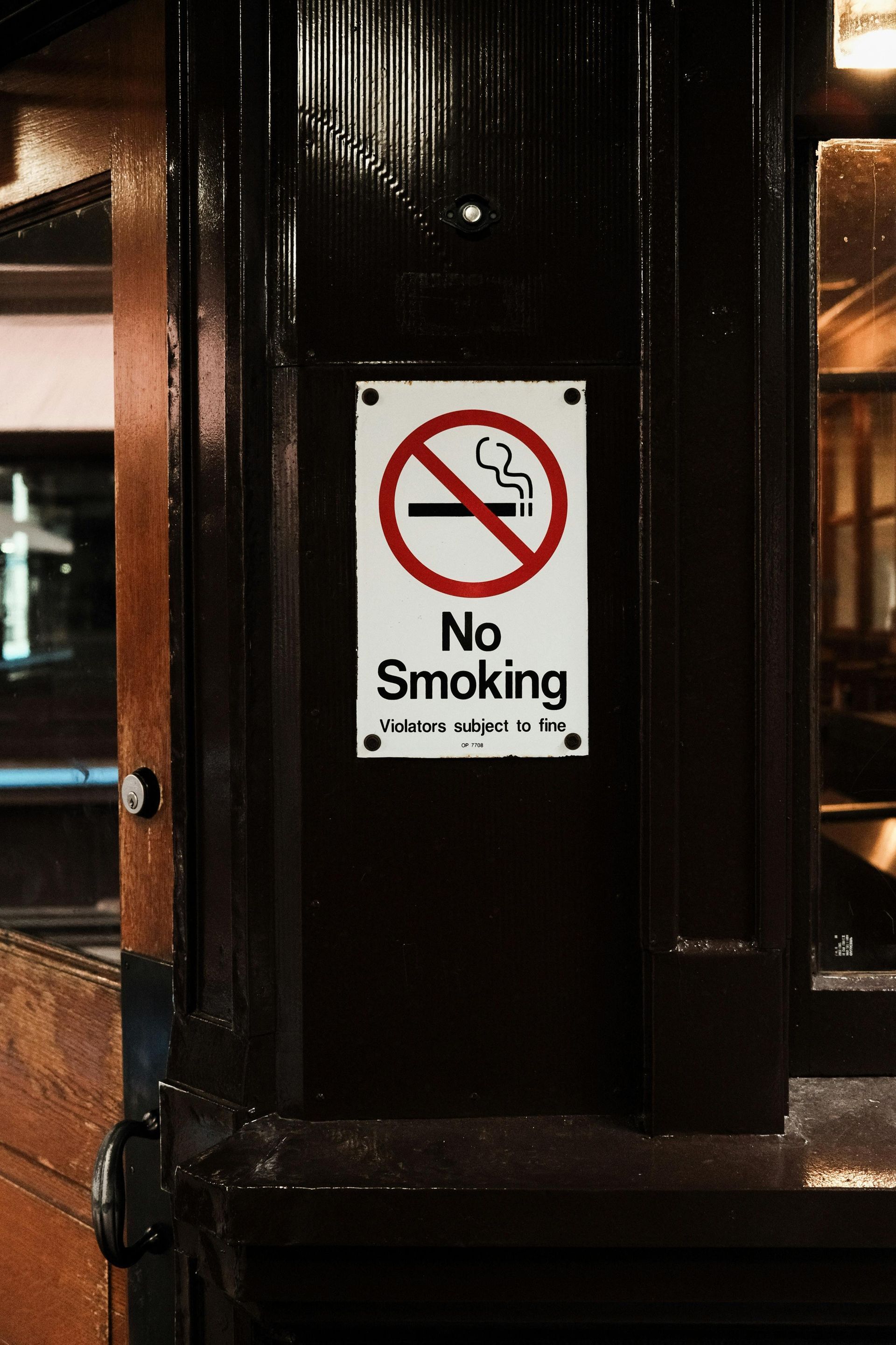 No smoking sign on a dark brown column, with text and a red crossed-out cigarette.
