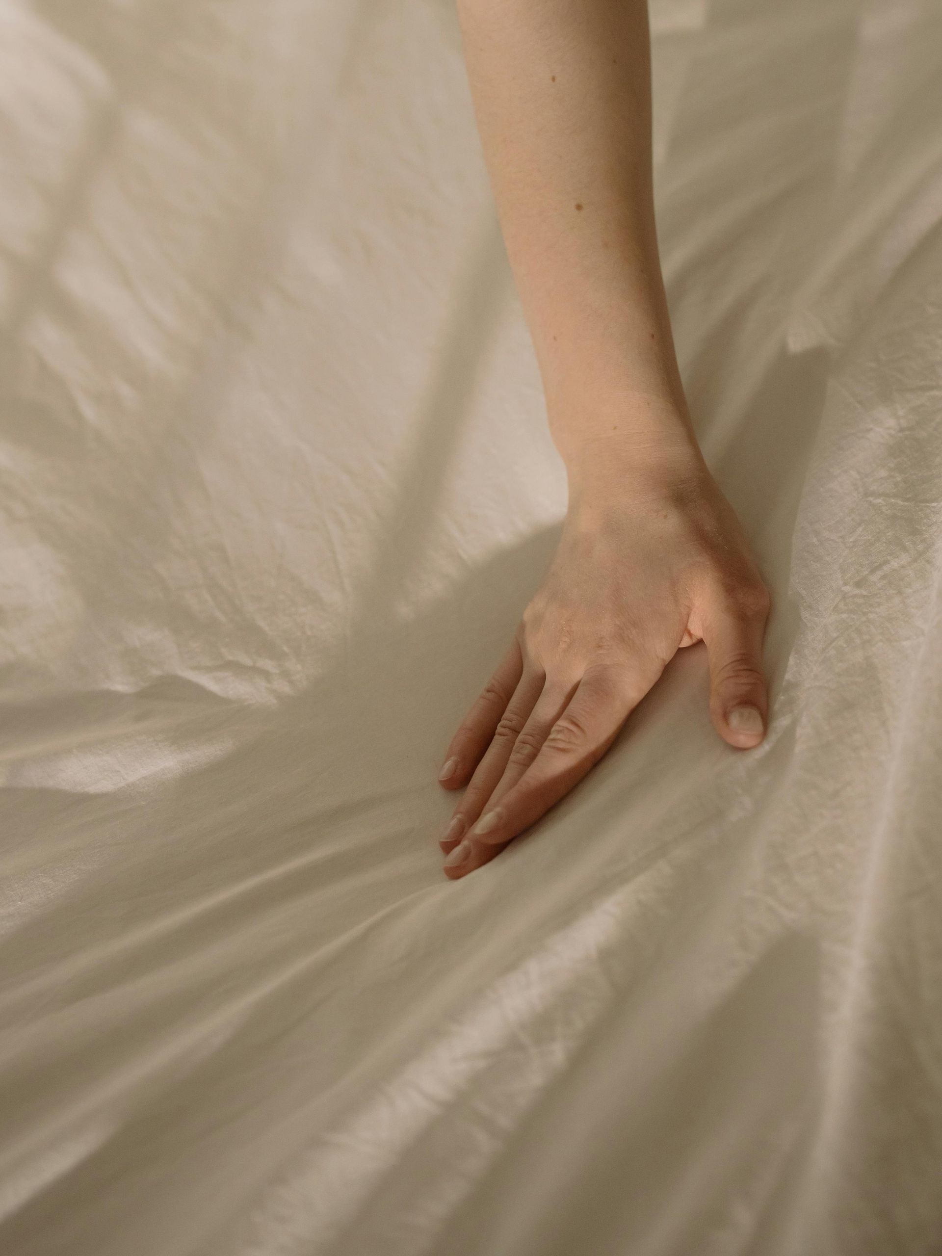 Hand resting on wrinkled white sheets.