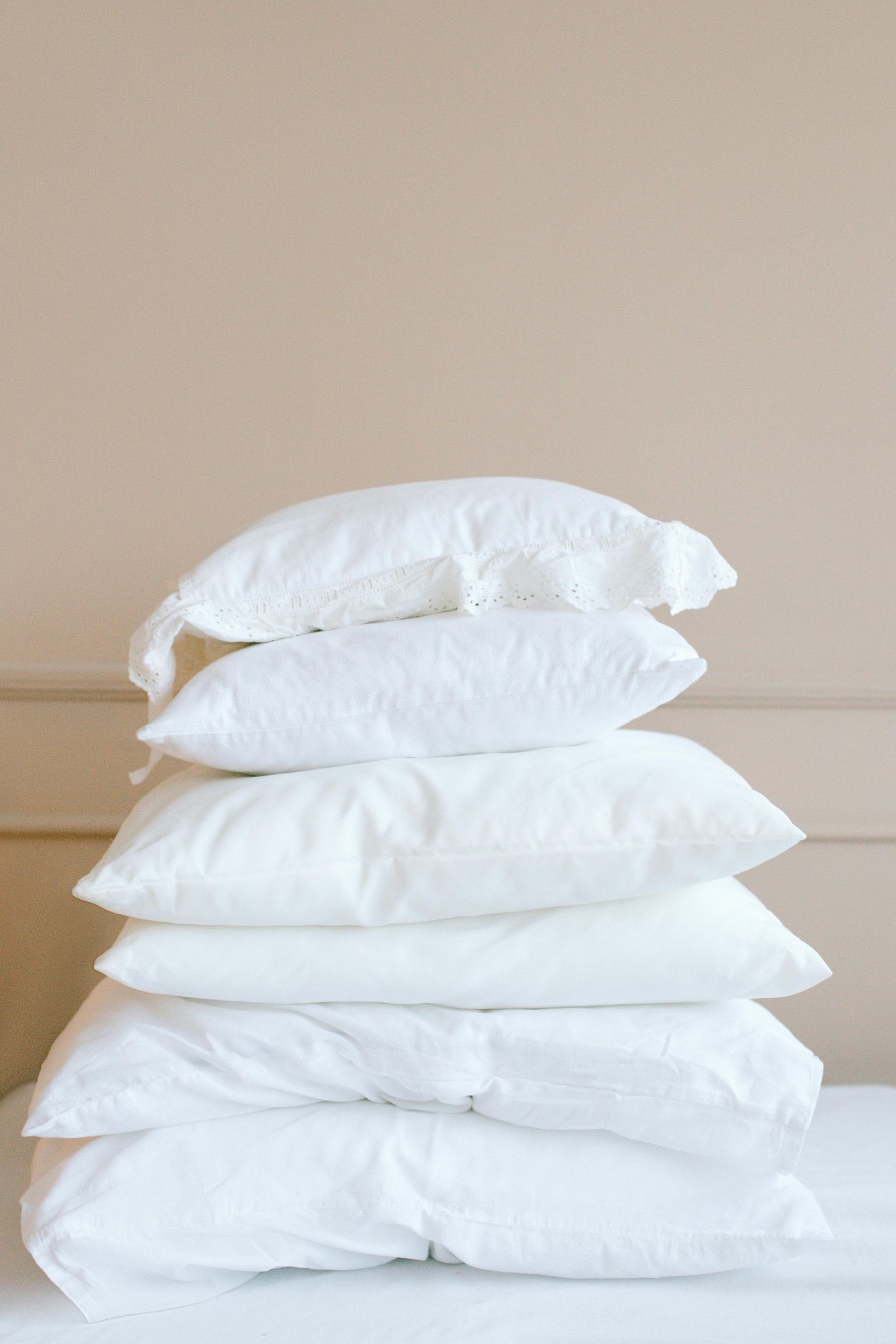 Pile of white pillows on a bed. Soft, fluffy, against a beige wall.