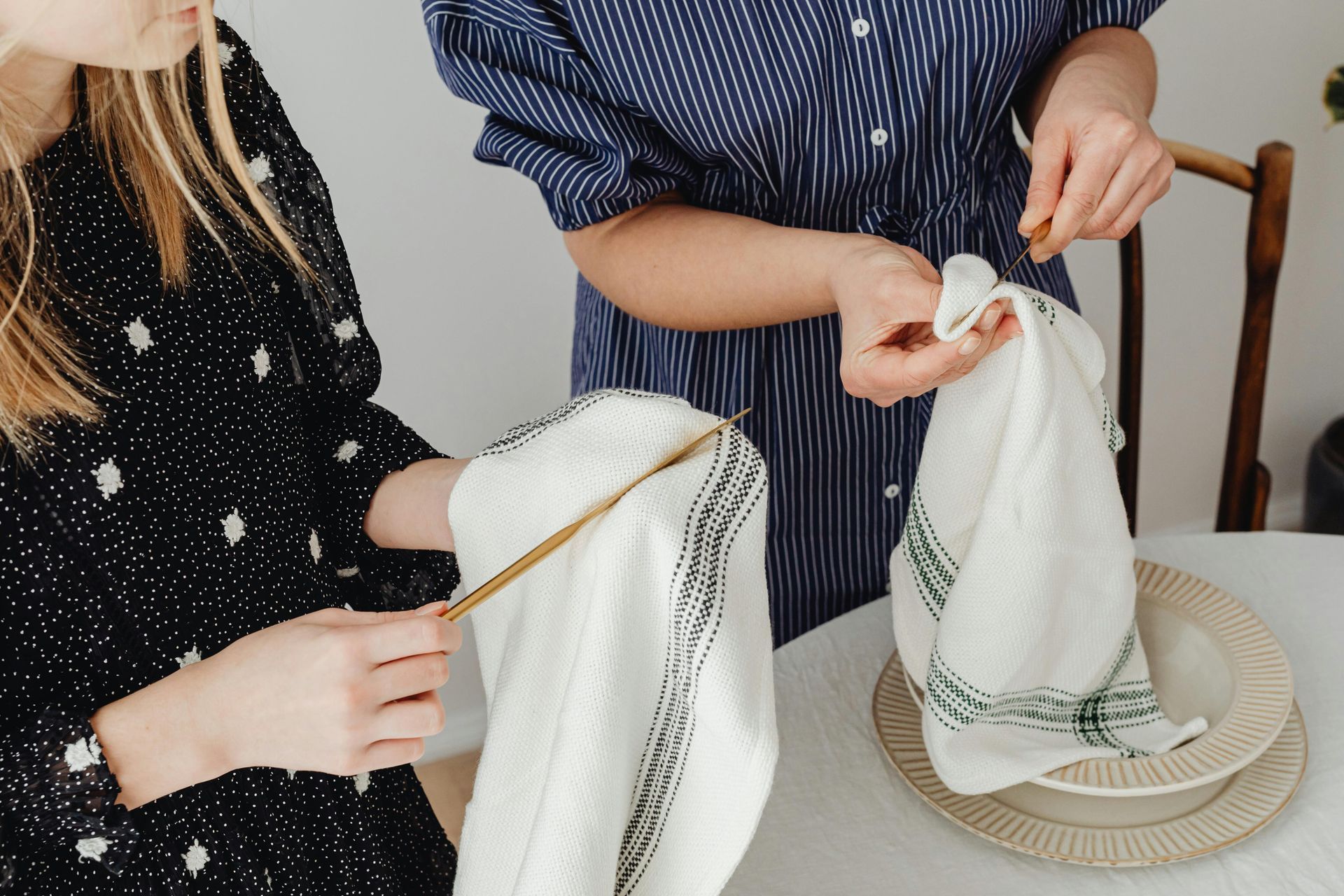 Two women are sitting at a table folding napkins.