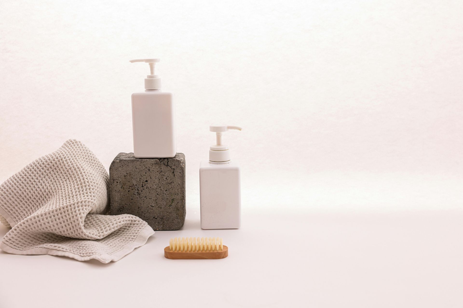 Two white soap dispensers, a towel, and a brush on a white surface.