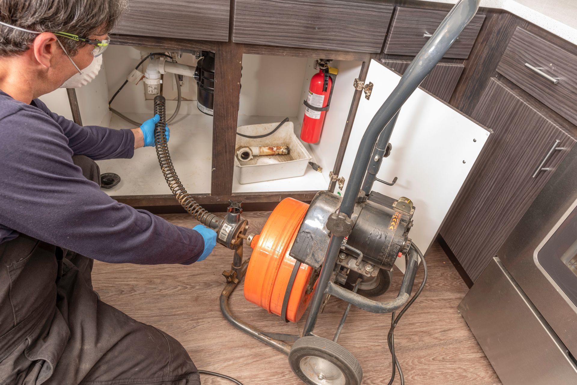 A plumber using an auger to clear a clogged household drain.
