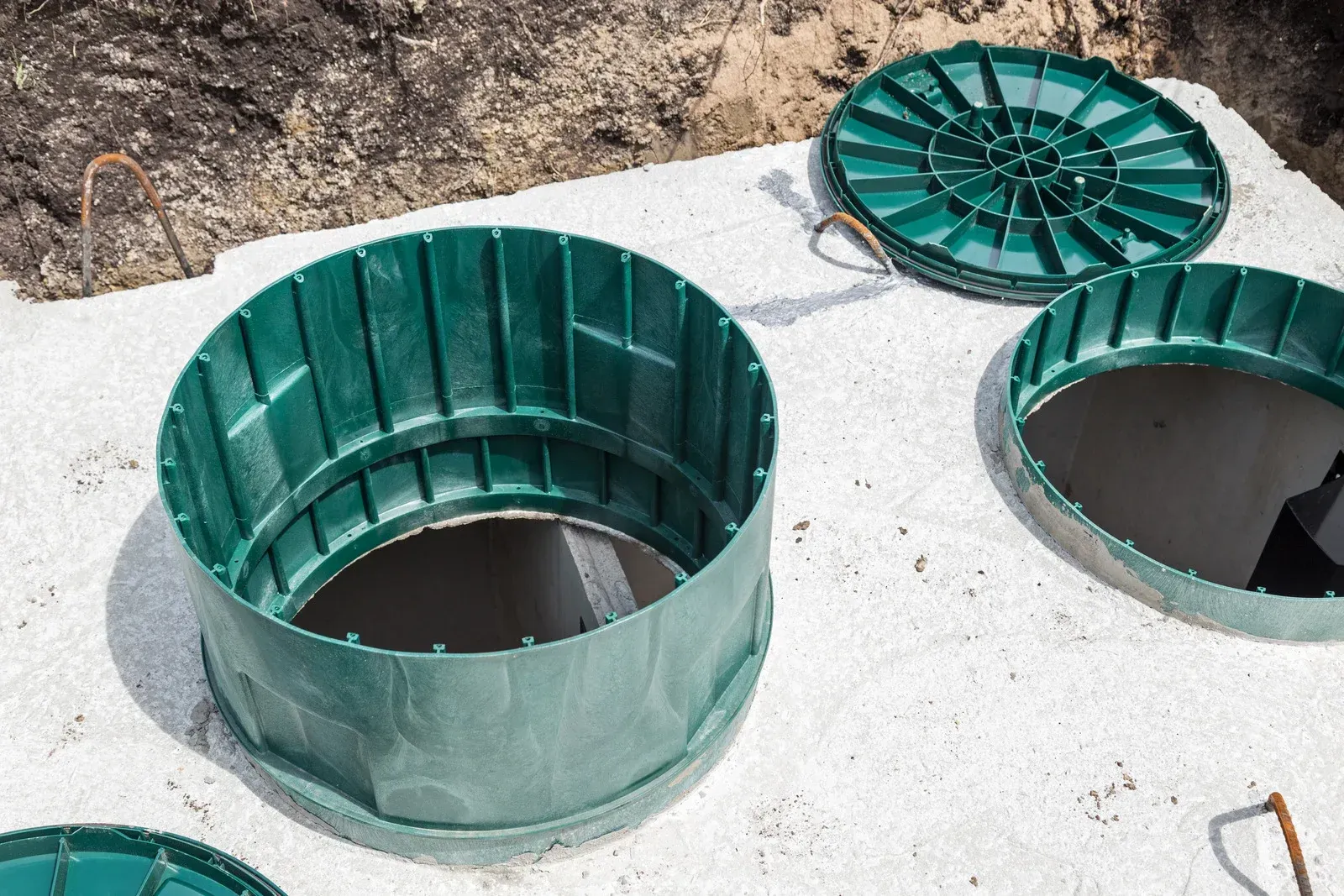 Three green septic tank lids, one open, in a shallow excavation with white gravel.