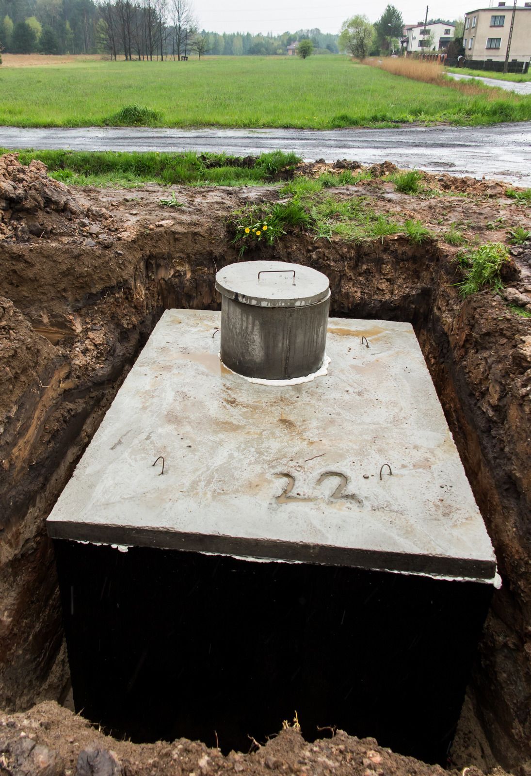 Concrete septic tank in an excavated pit, with a field and road in the background.