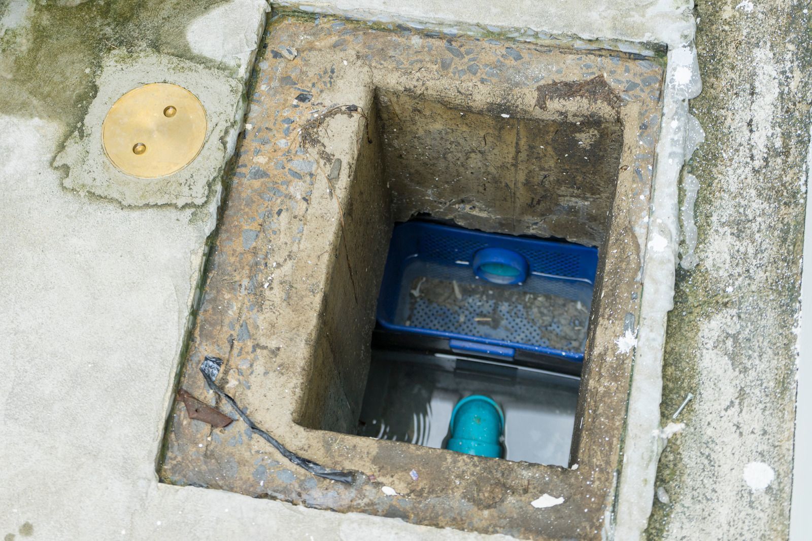 Open concrete drain with a blue basket inside and a pipe at the bottom.