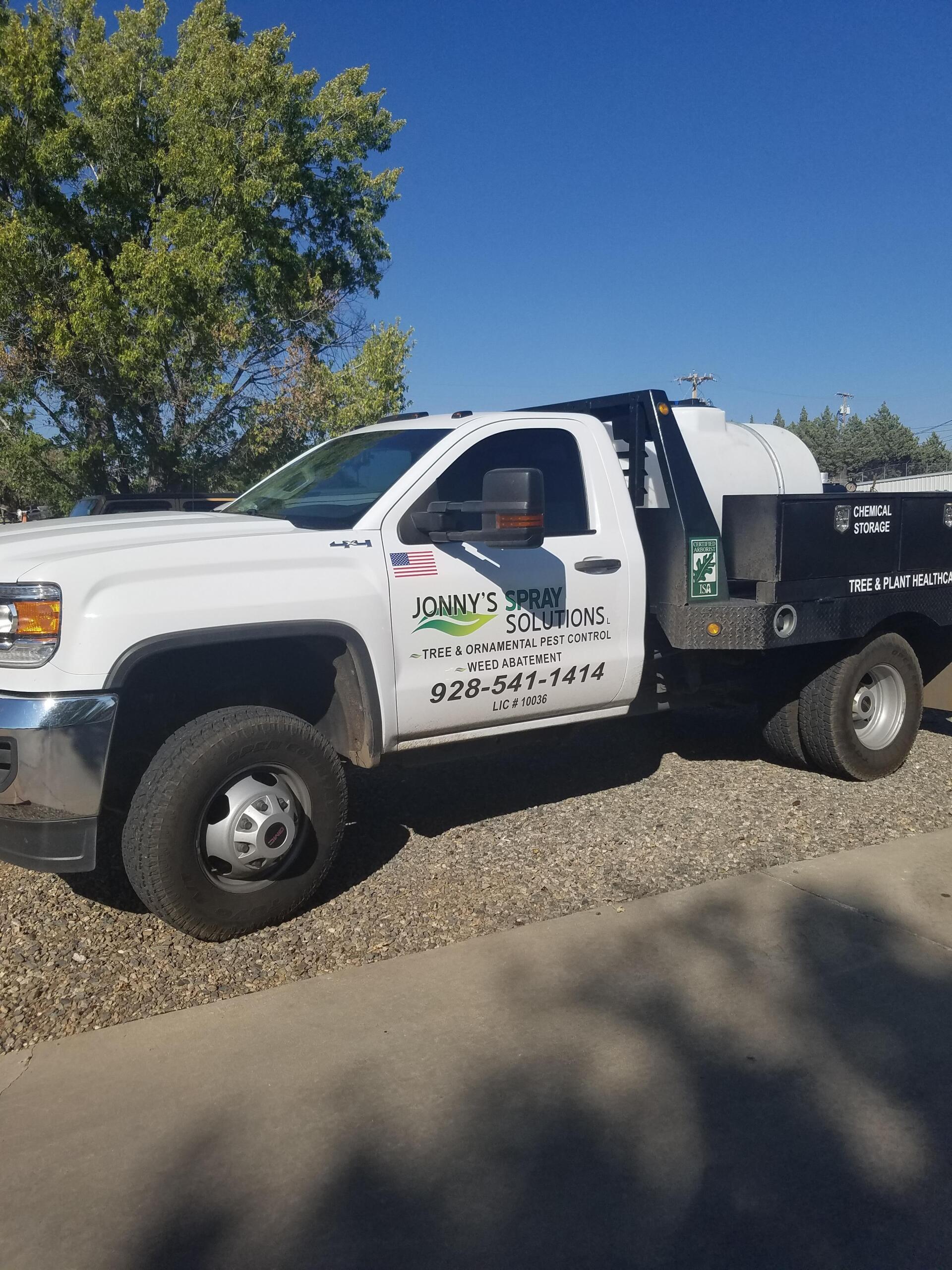 White work truck with a flatbed, parked on gravel. 