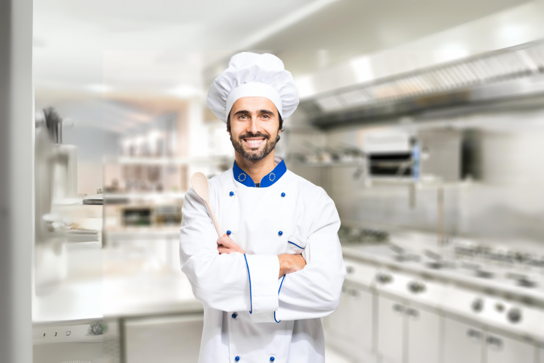 A chef is standing in a kitchen with his arms crossed.