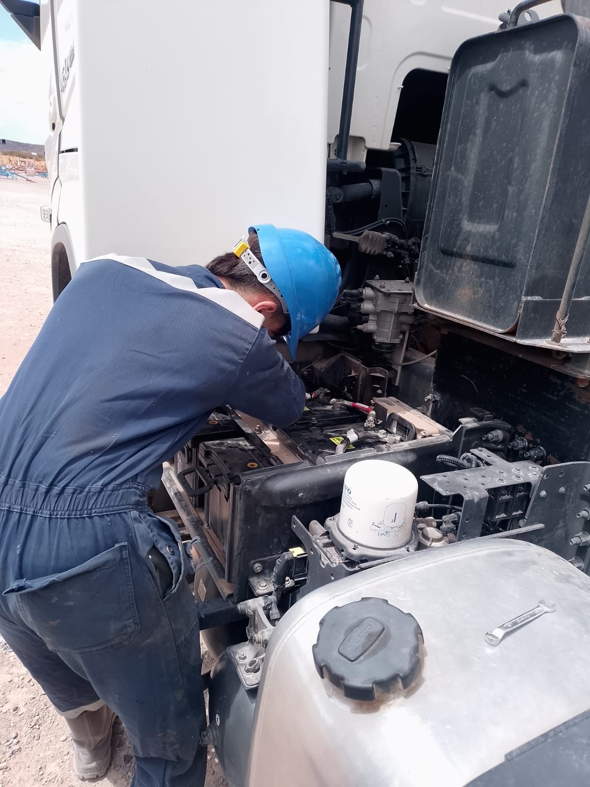 Persona con guantes conectando cables de arranque a la batería de un coche bajo el capó.