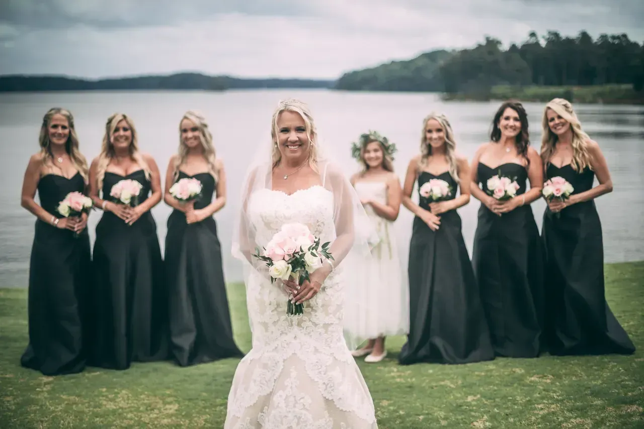 A bride and her bridesmaids are posing for a picture in front of a lake.