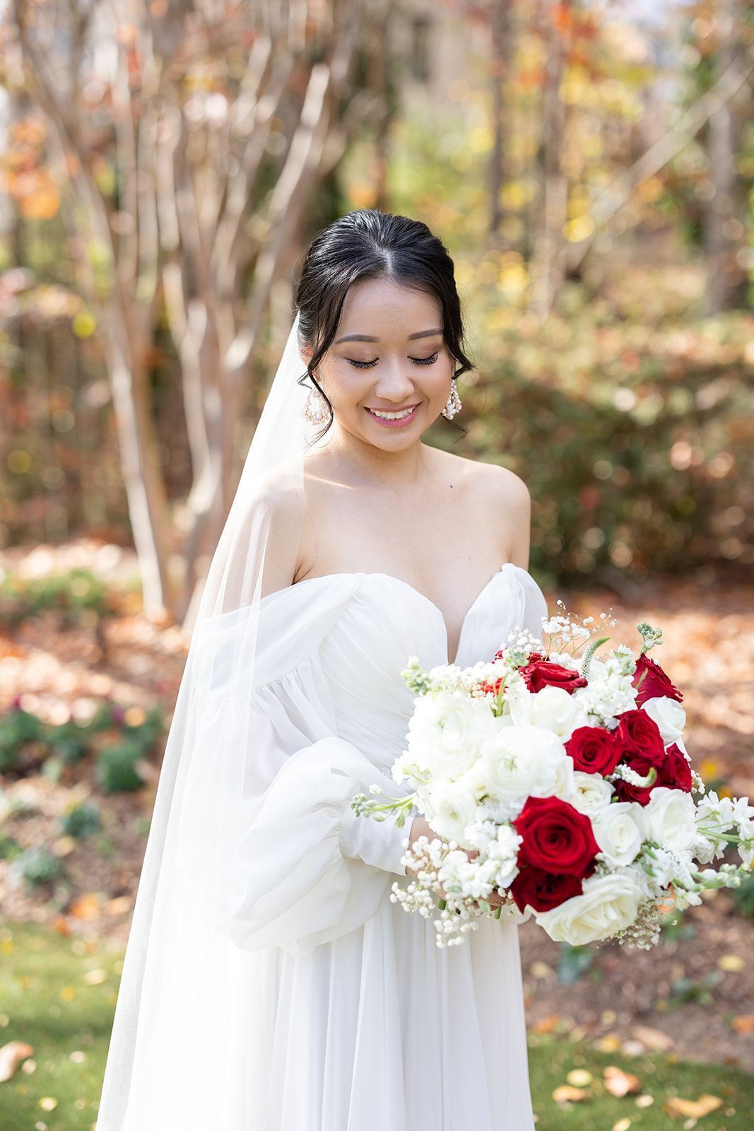 A bride in a white dress is holding a bouquet of red and white flowers.