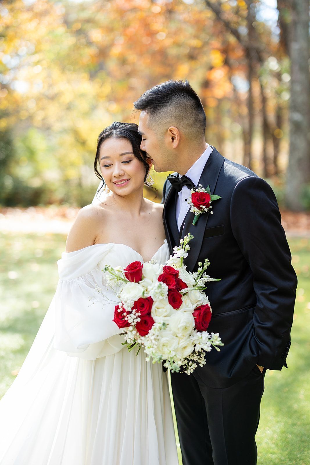 A bride and groom are posing for a picture and the groom is kissing the bride on the cheek.