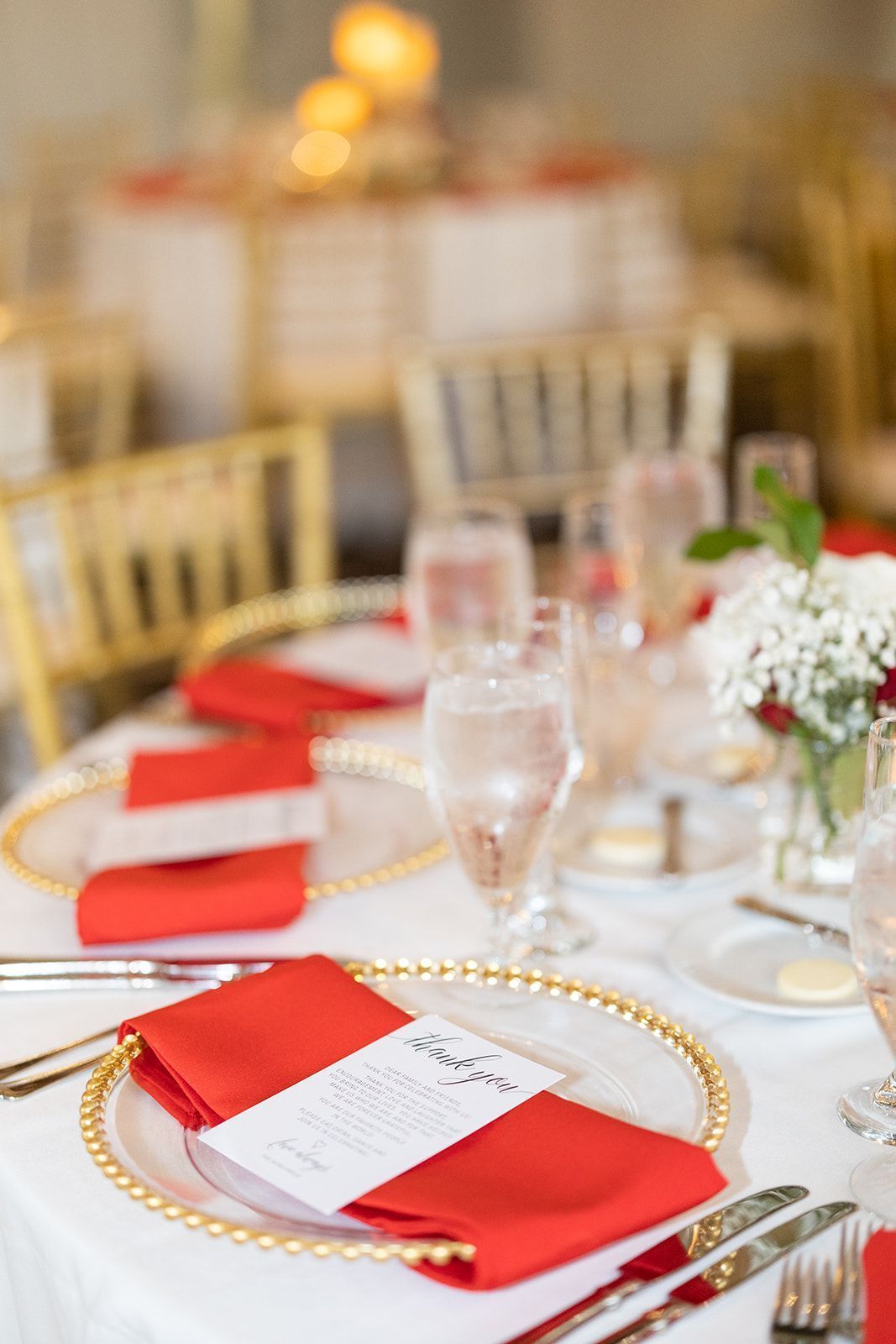 A table set for a wedding reception with red napkins and gold plates.