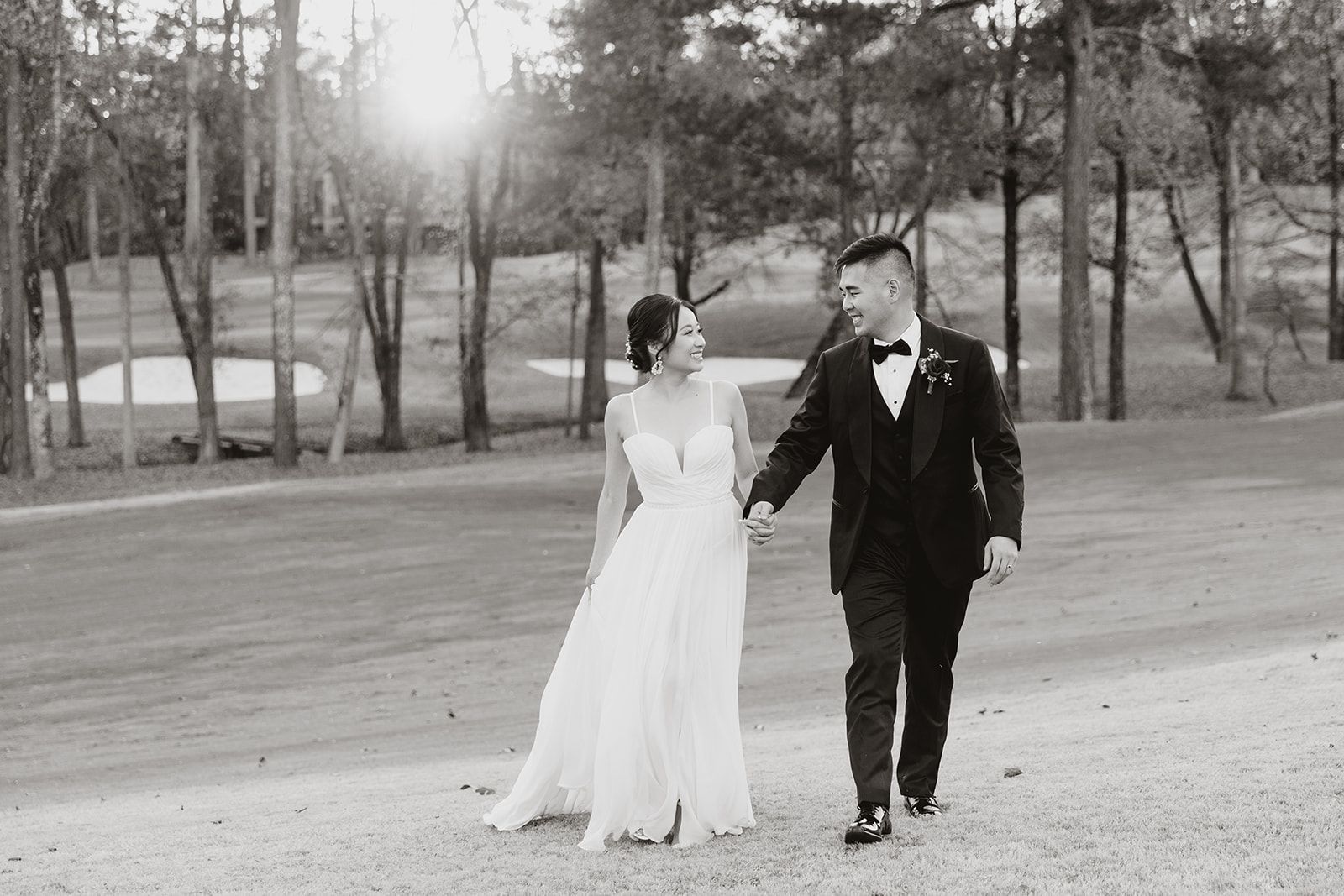 A bride and groom are walking down a dirt road holding hands.