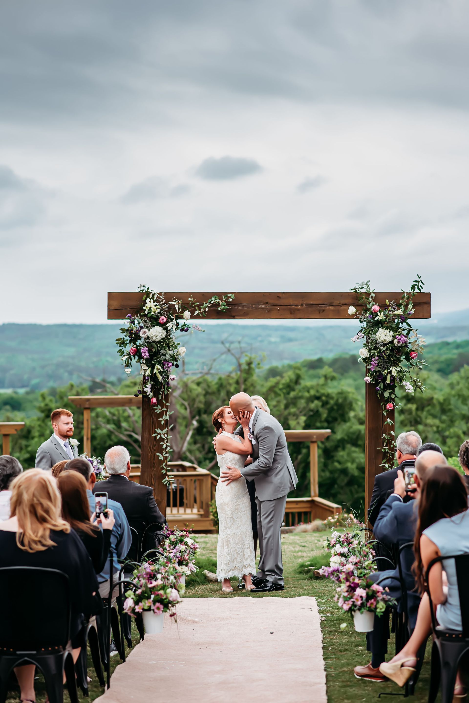 A bride and groom are kissing at their wedding ceremony while their guests watch.