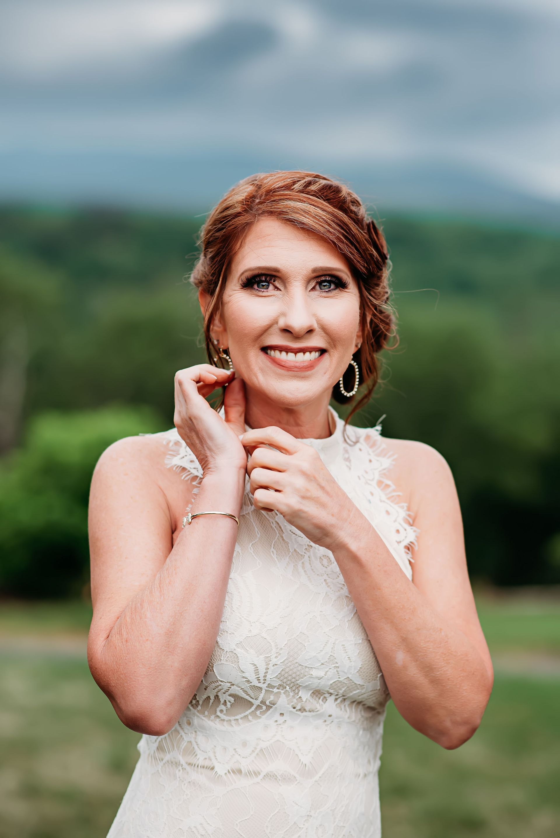 A woman in a wedding dress is smiling and putting on her earrings.