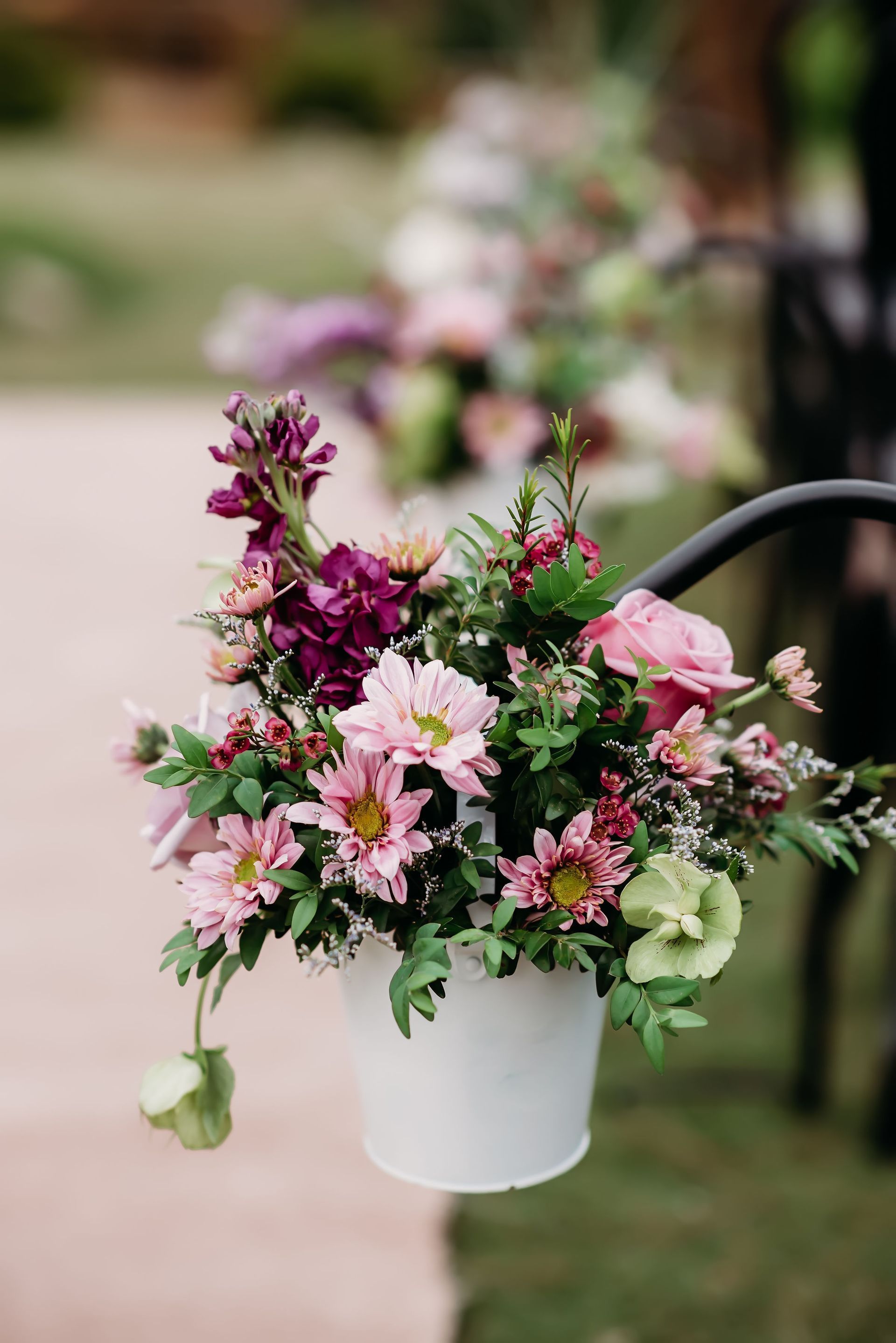 A white pot filled with pink and purple flowers is hanging from a pole.