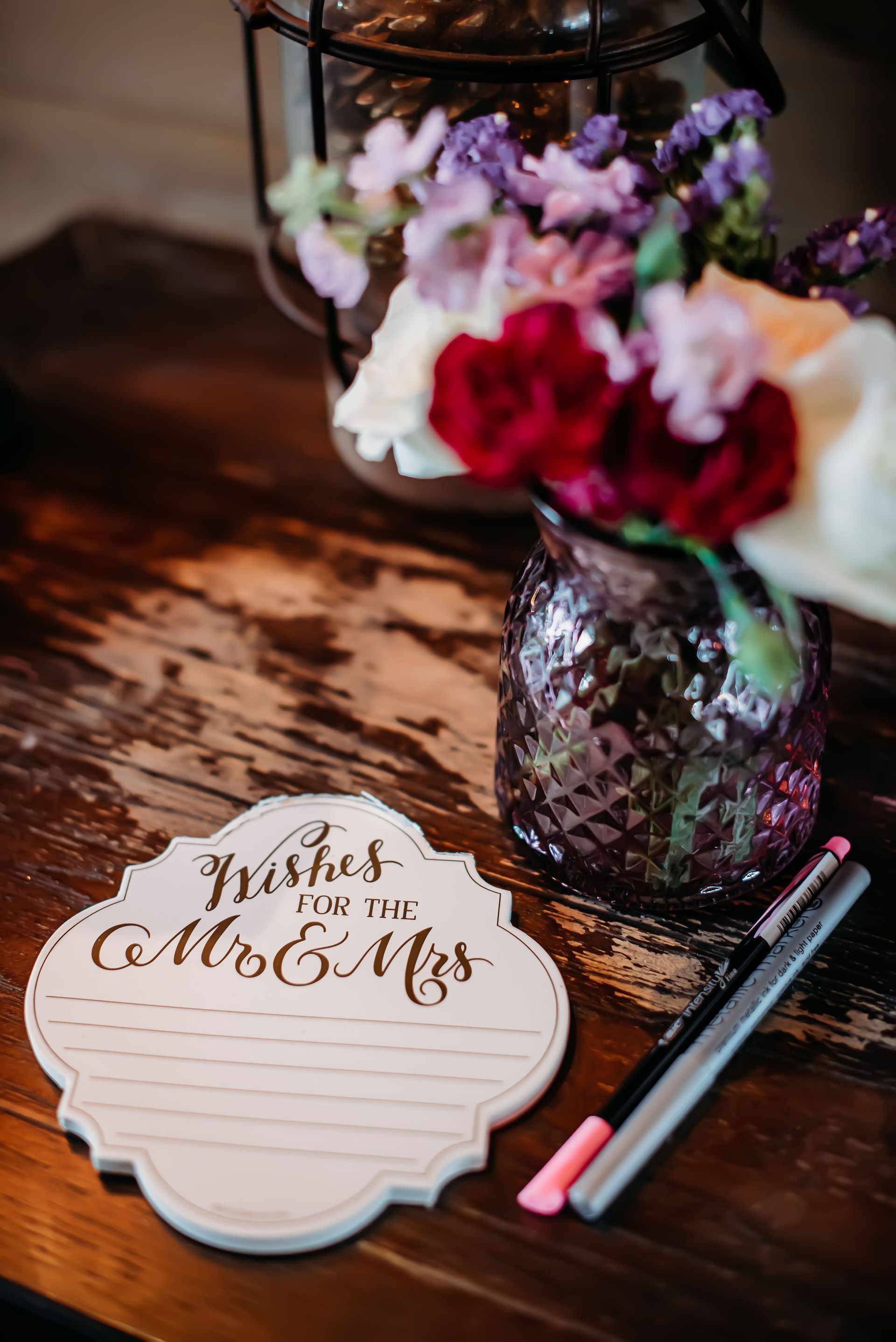 A vase of flowers is sitting on a wooden table next to a sign and pens.