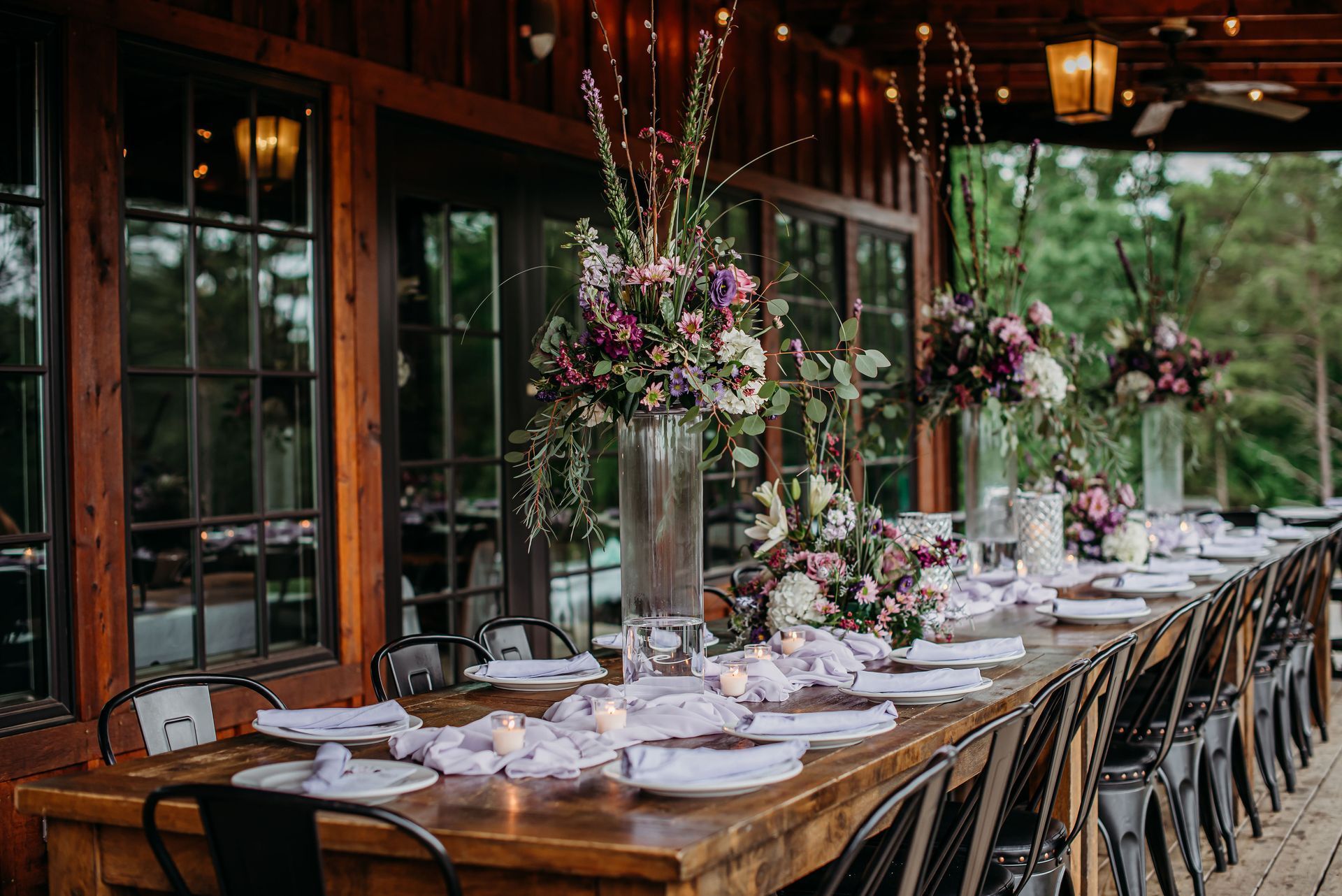 A long wooden table is set for a wedding reception with flowers in vases.