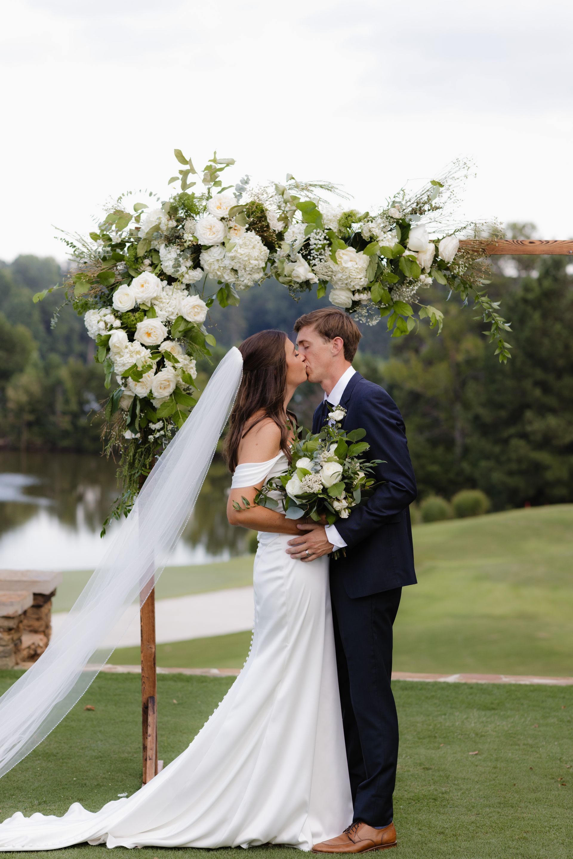 A bride and groom kissing under a floral arch at their wedding.