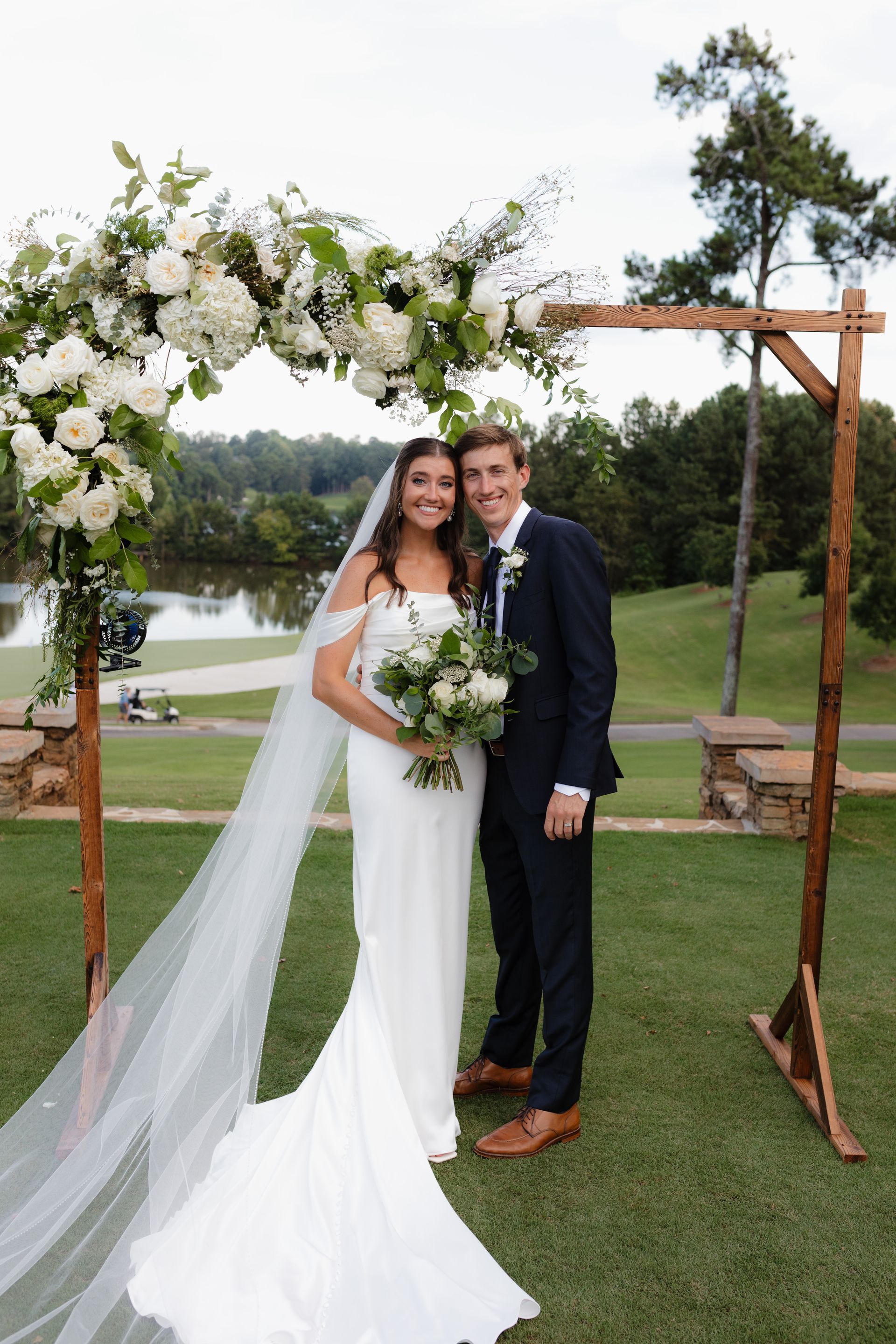 A bride and groom are posing for a picture in front of a wooden arch.