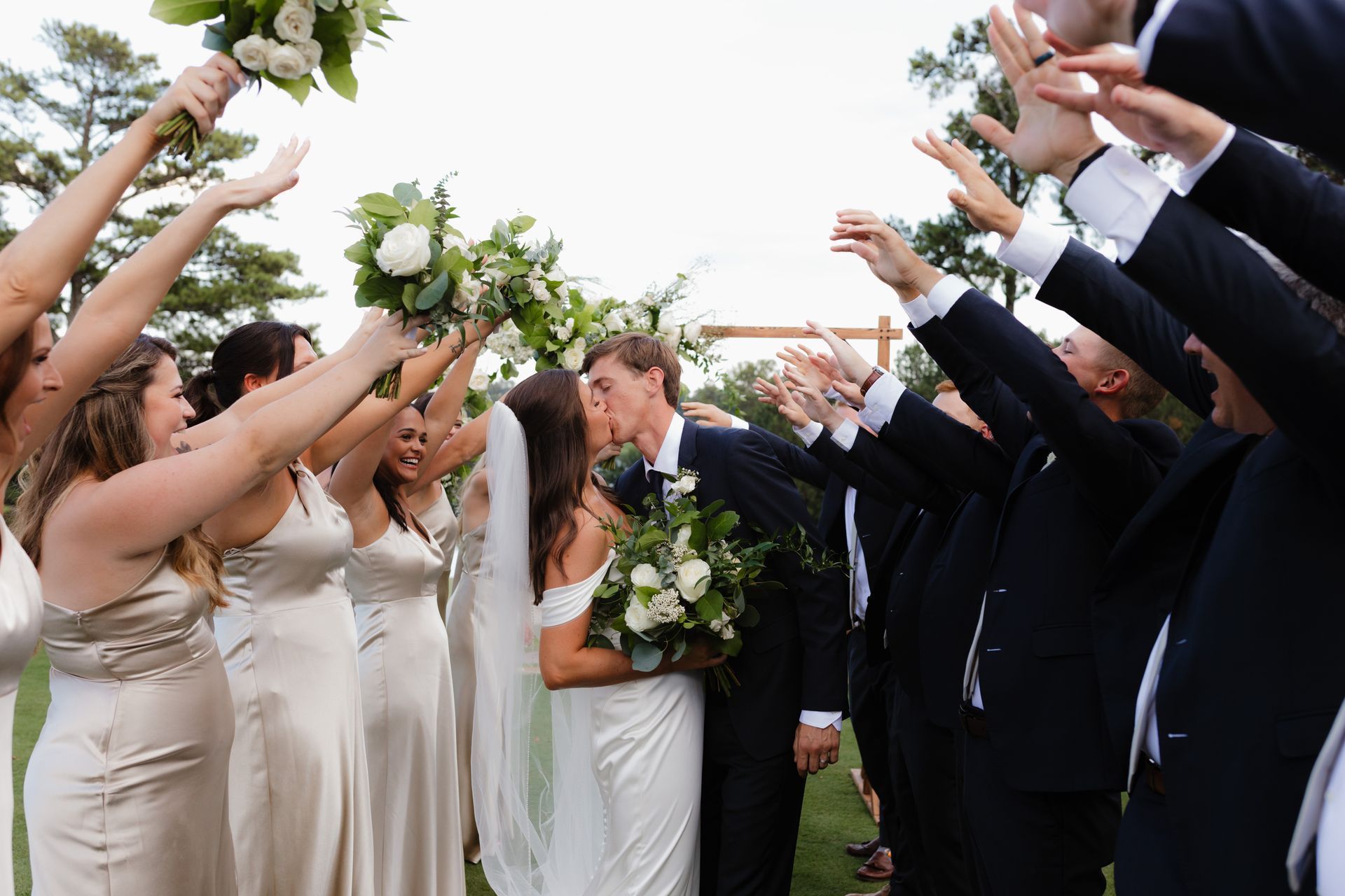 A bride and groom are kissing while their wedding party throws flowers in the air.