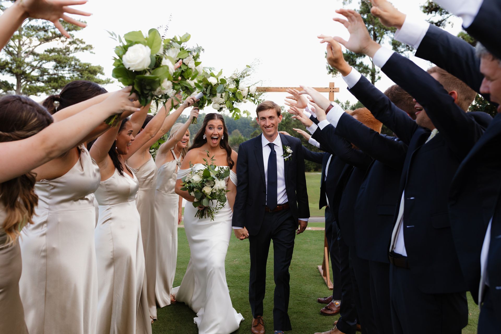 A bride and groom are walking through a tunnel of their wedding party.