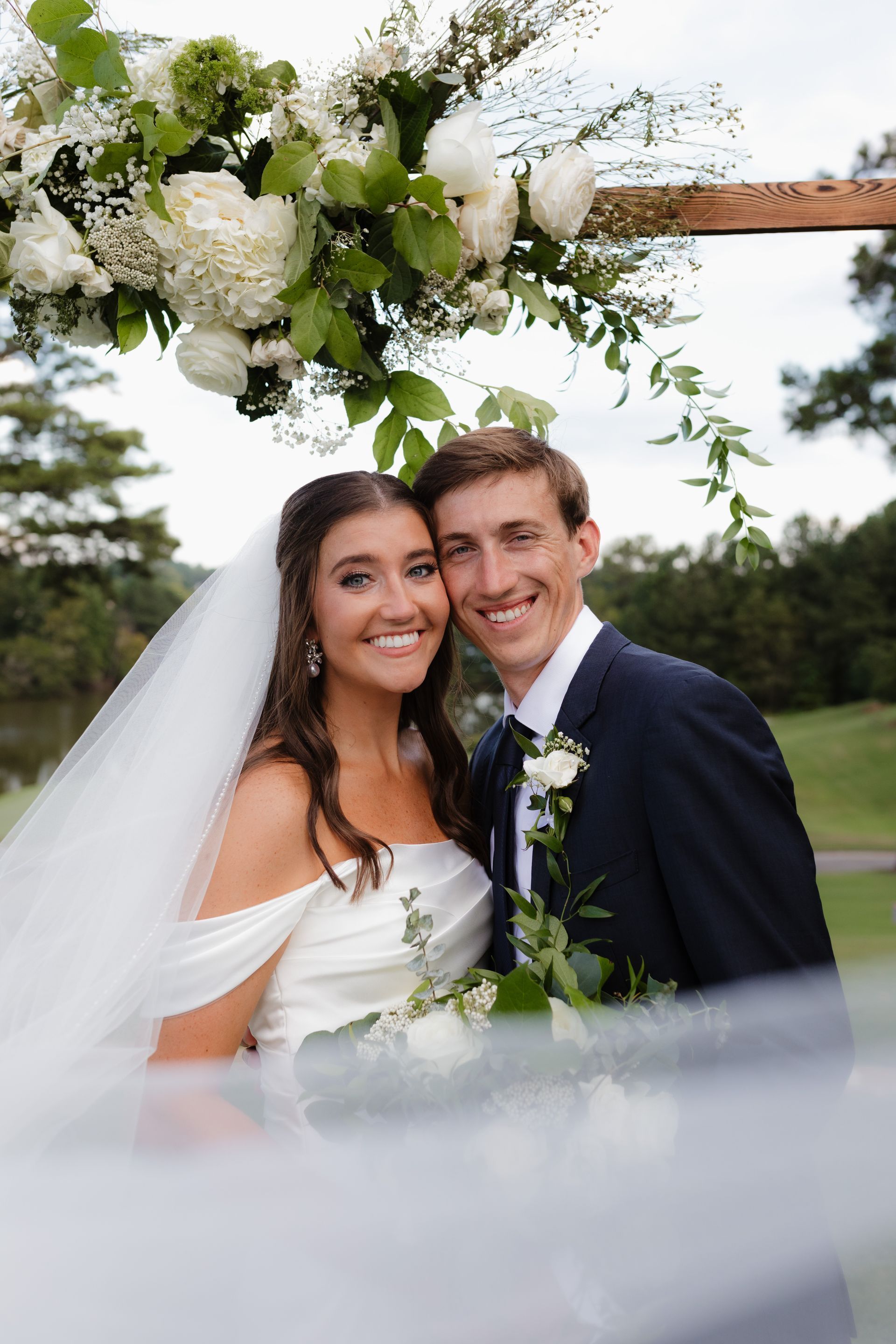 A bride and groom are posing for a picture under a floral arch.