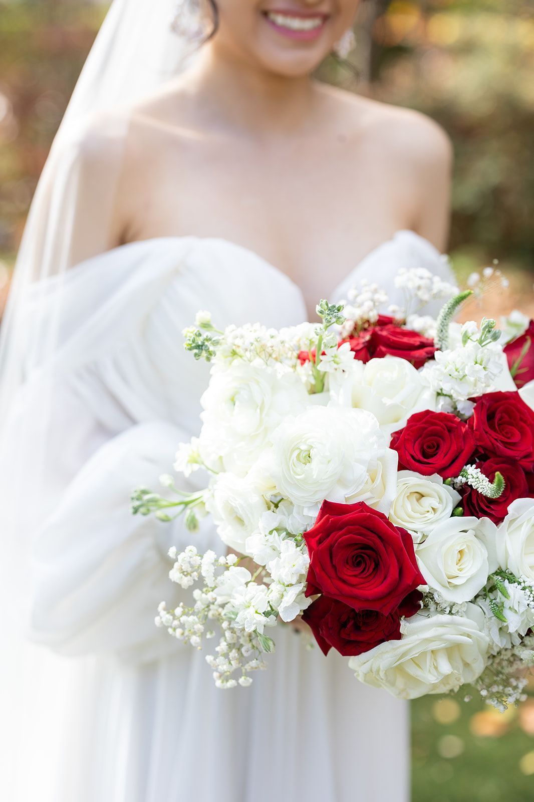 A bride in a white dress is holding a bouquet of red and white flowers.