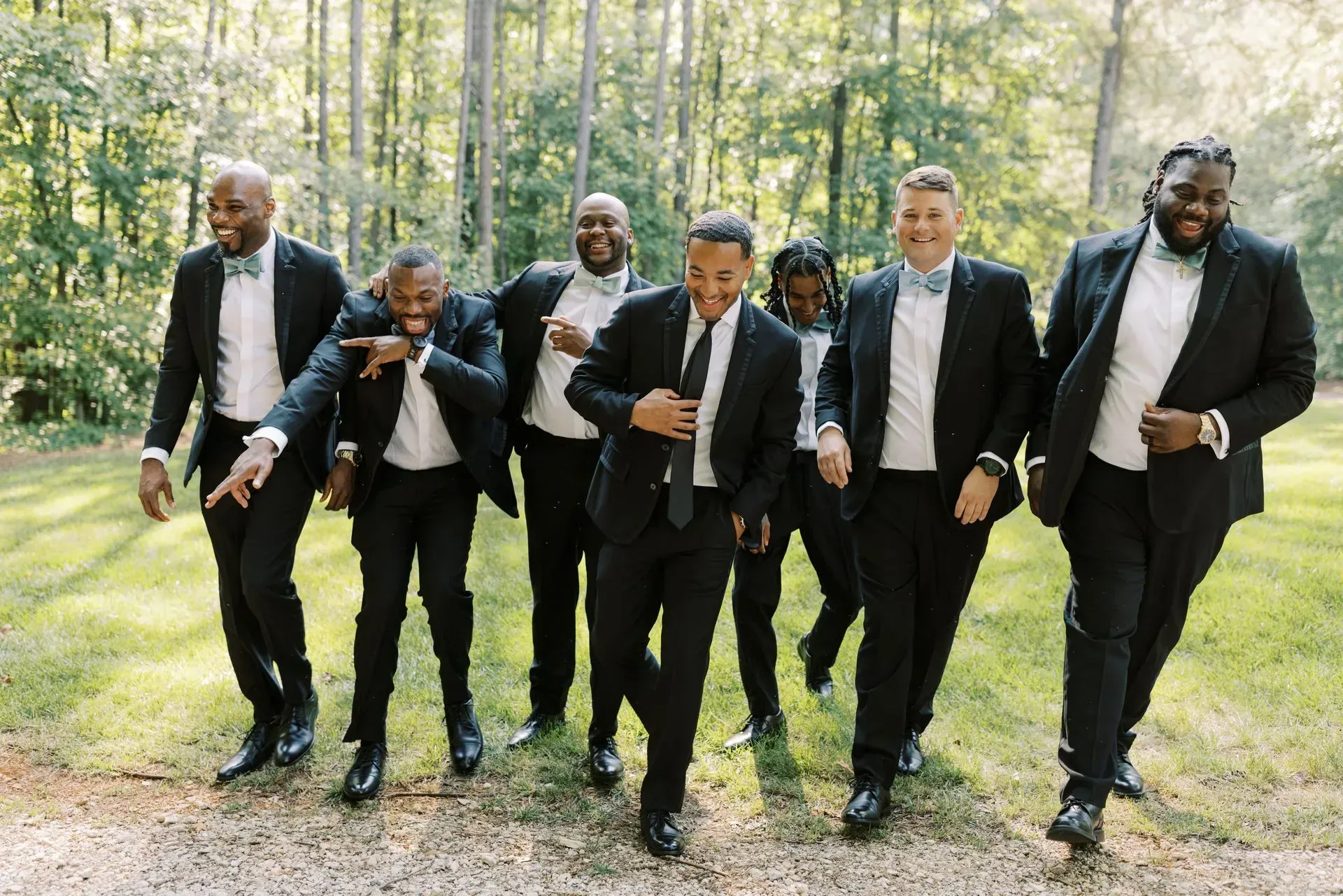 A group of men in suits and bow ties are walking in the woods.