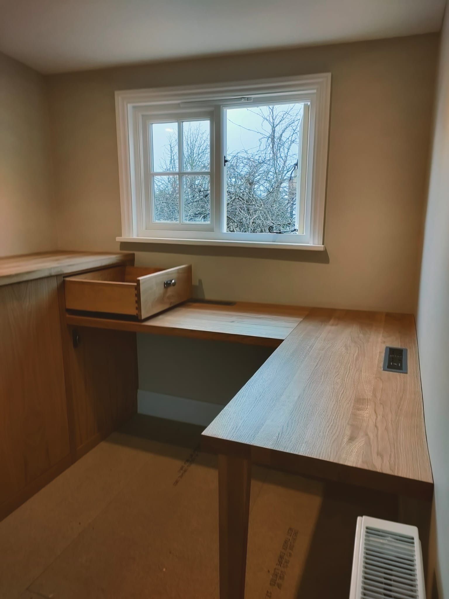 A wooden desk with a drawer underneath it in a room with a window.