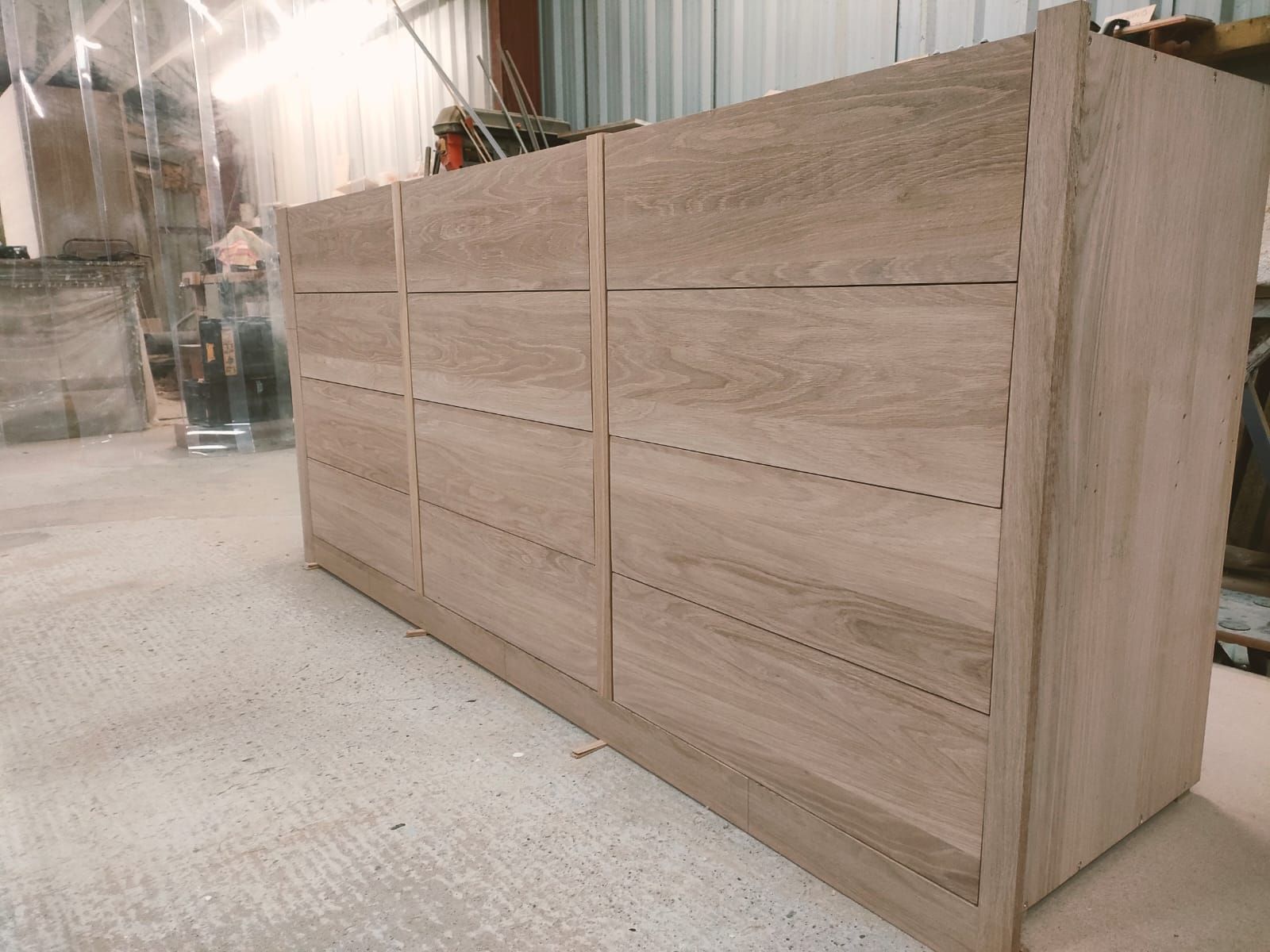 A wooden dresser with six drawers arranged in two columns, shown in an unfinished state inside a workshop.